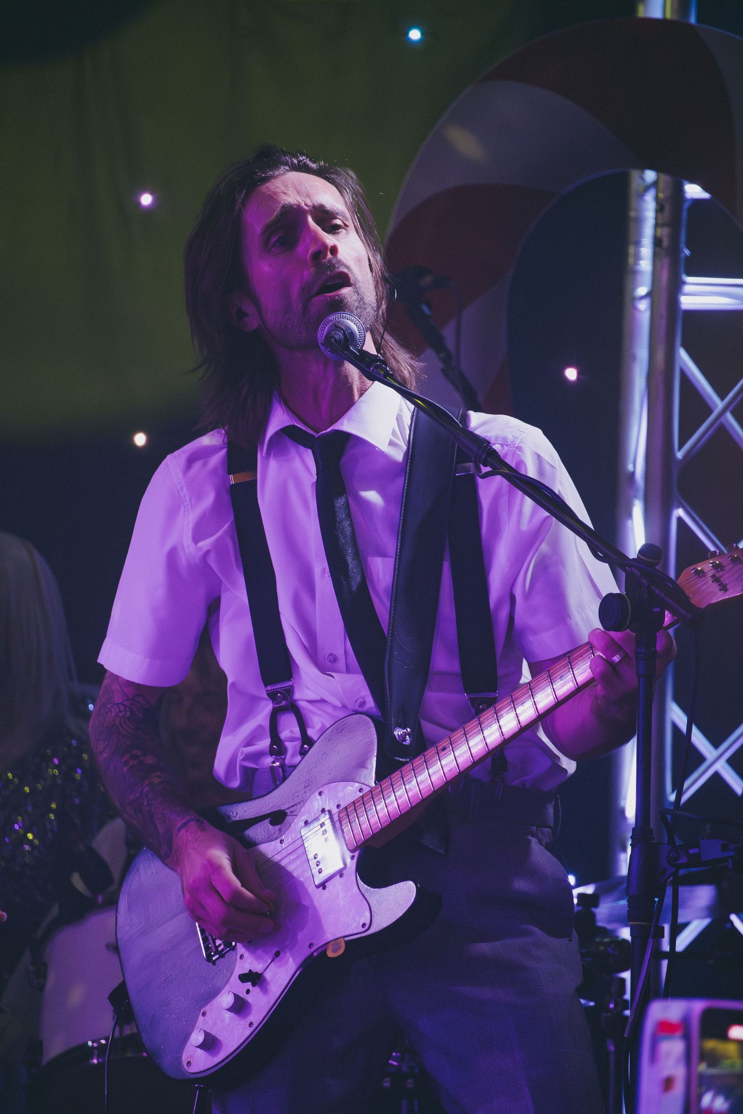 Guitar player performs energetically on stage under dramatic purple lighting.