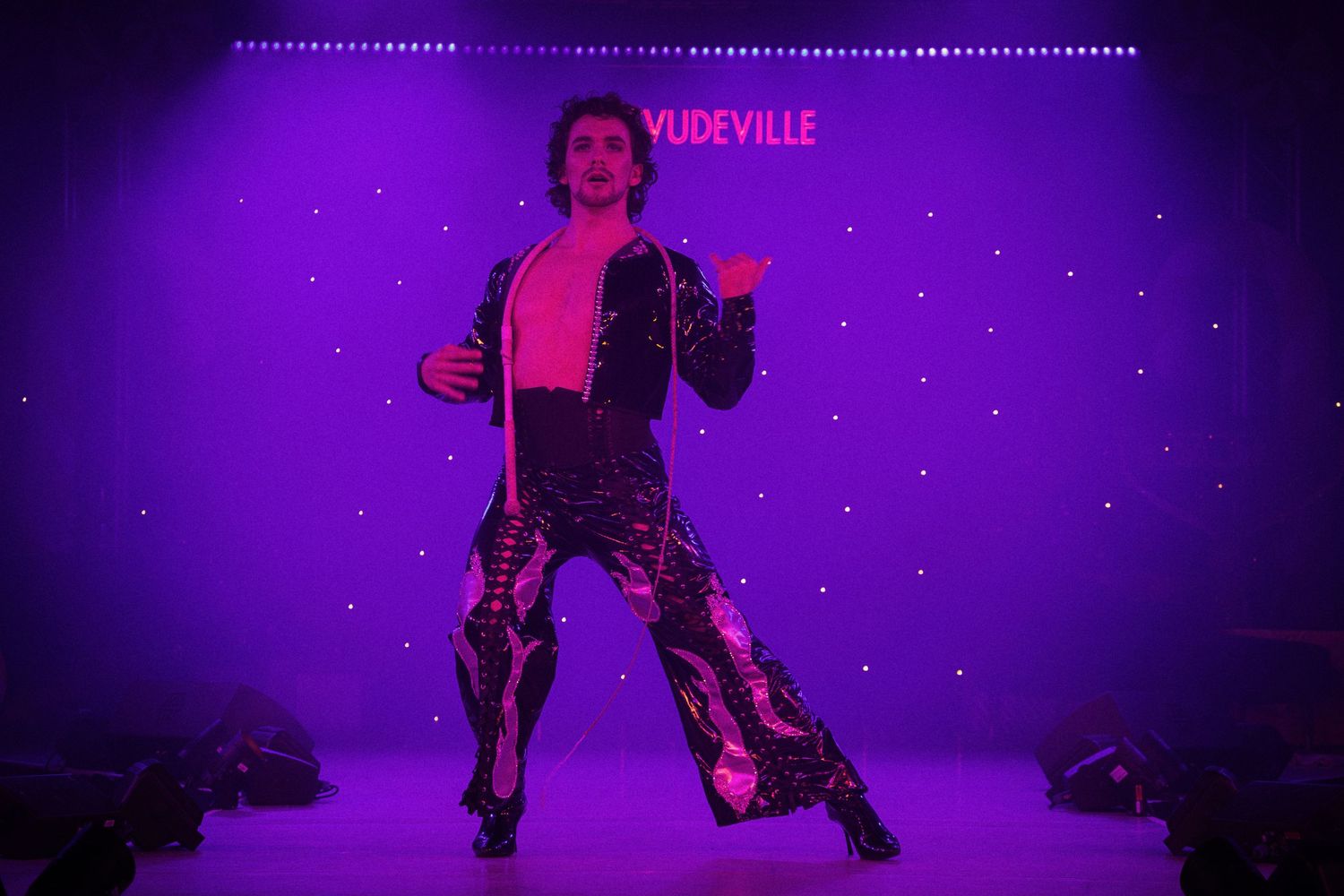 Performers dance on stage during a burlesque show with dramatic purple lighting and sparkly costumes.