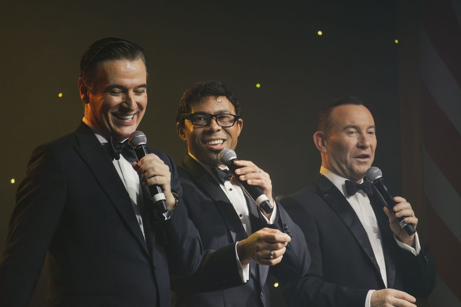 Group of performers in black suits entertain on darkened stage.