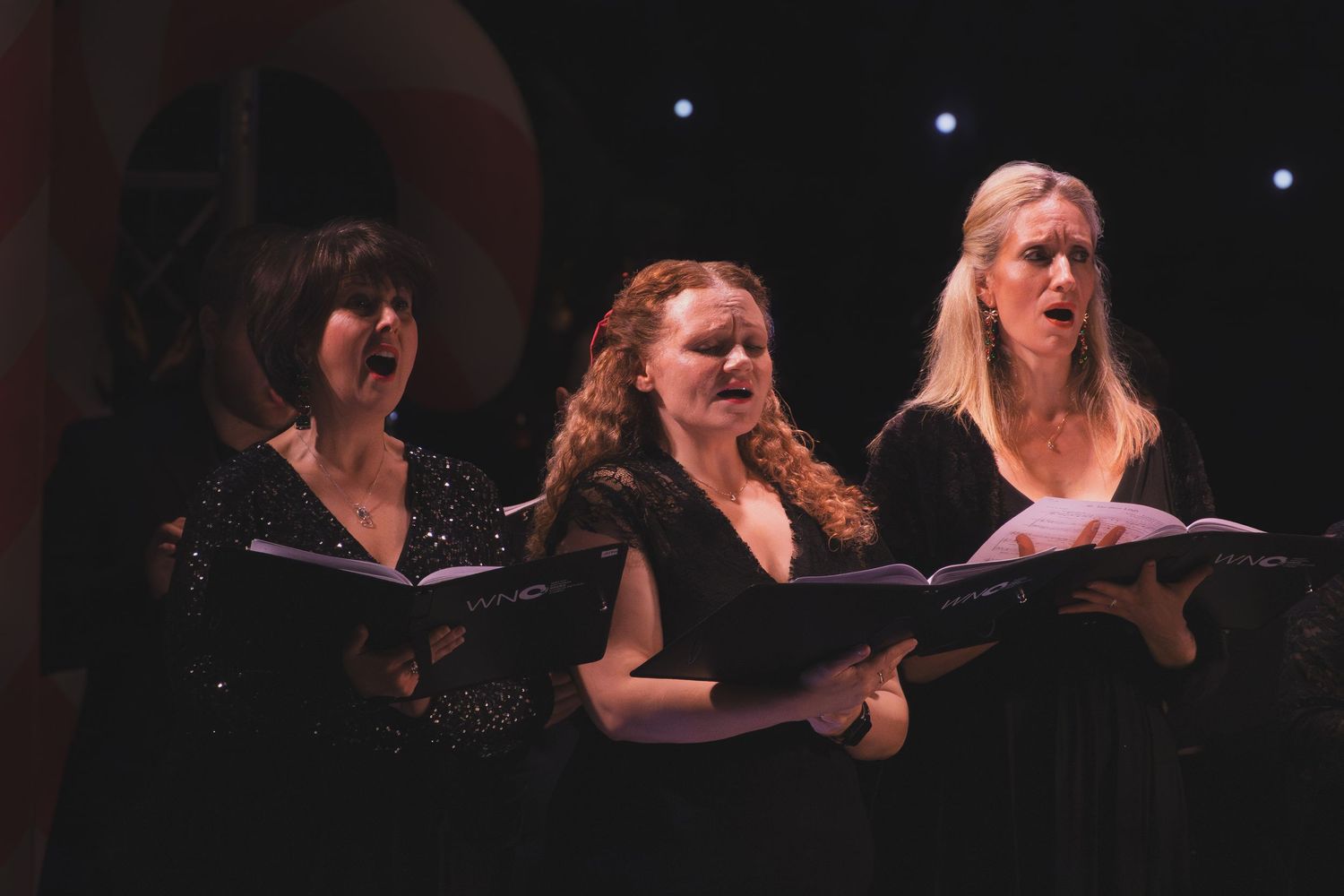 A group of vocalists in dark clothing perform together on a dimly lit stage.