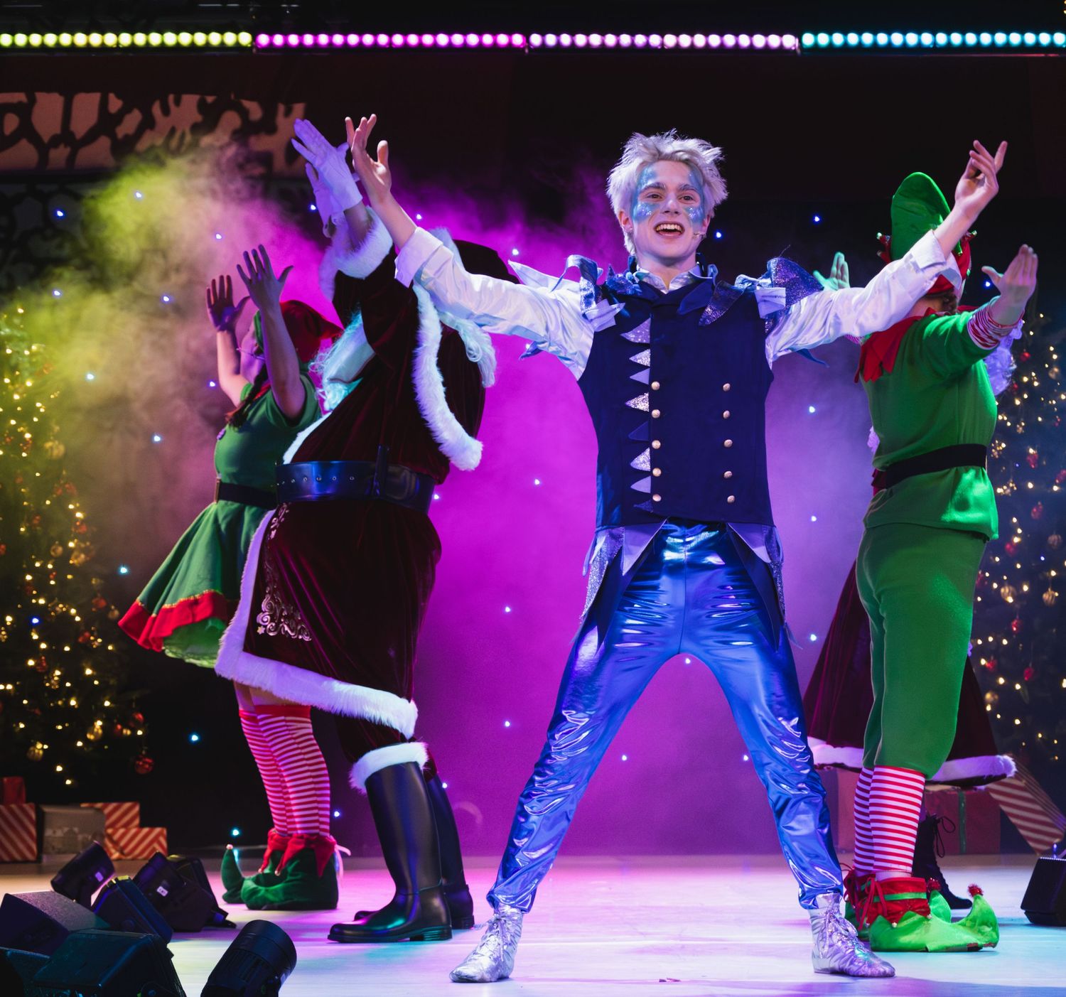 Colorful stage performance featuring dancers in holiday costumes under vibrant lighting effects.