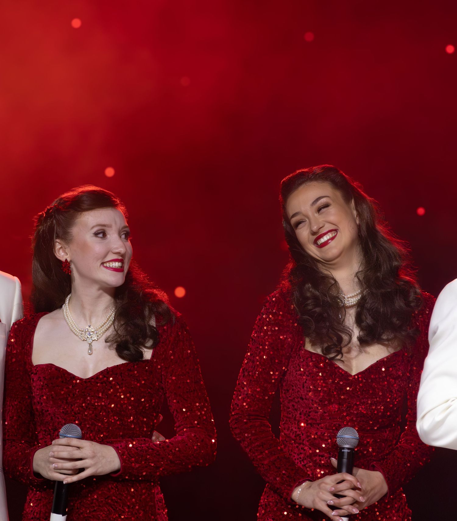 Performers in sparkly red costumes share a joyful moment during stage show.