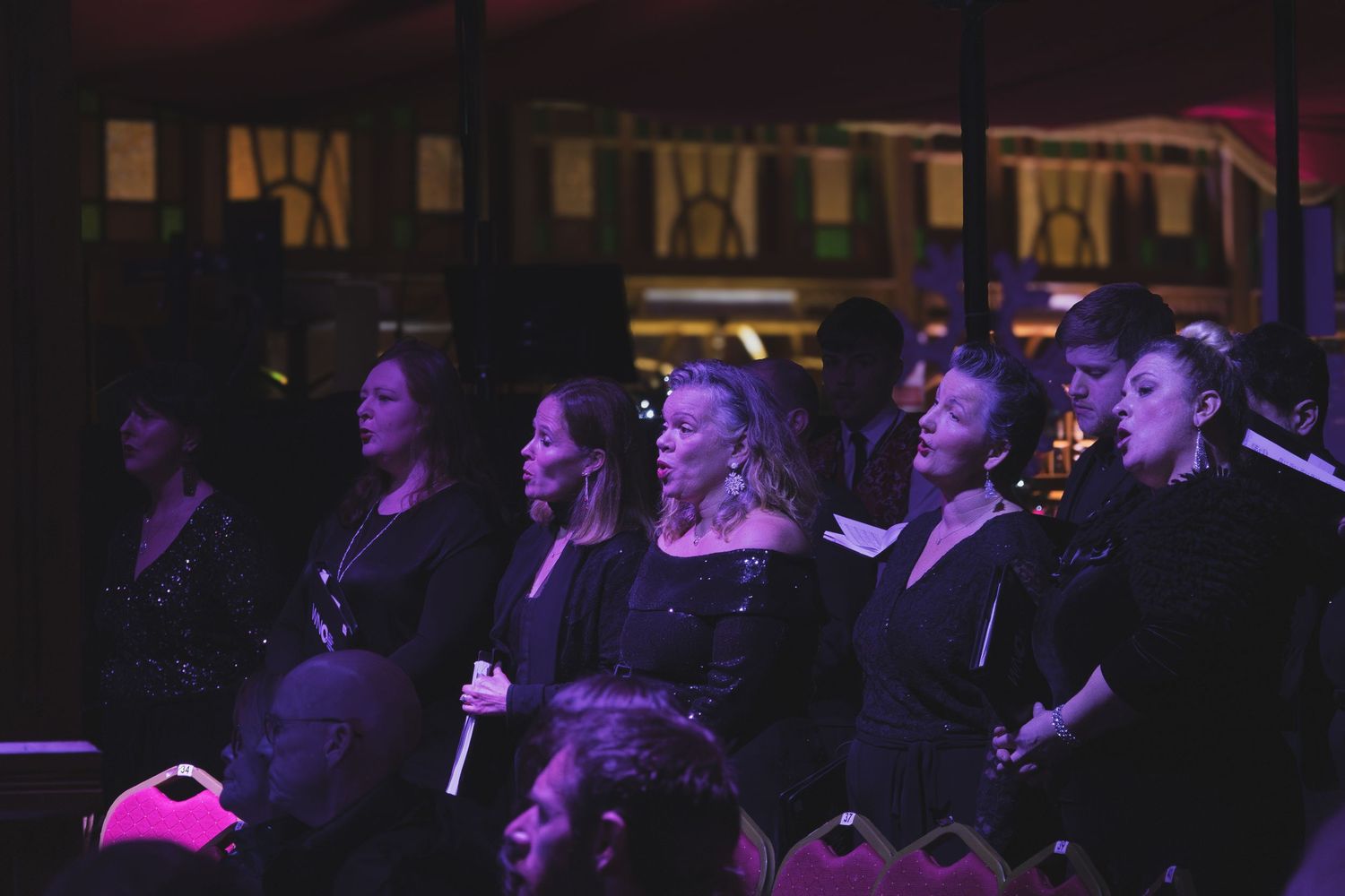 Concert audience watching a performance in a dimly lit venue with purple lighting.