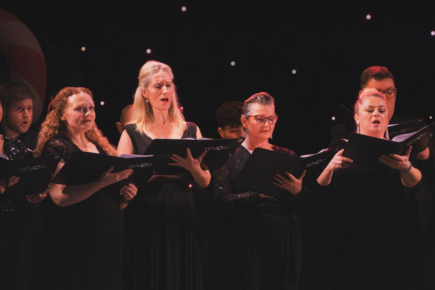 Choir ensemble singing together during a dramatic performance with spotlighting.
