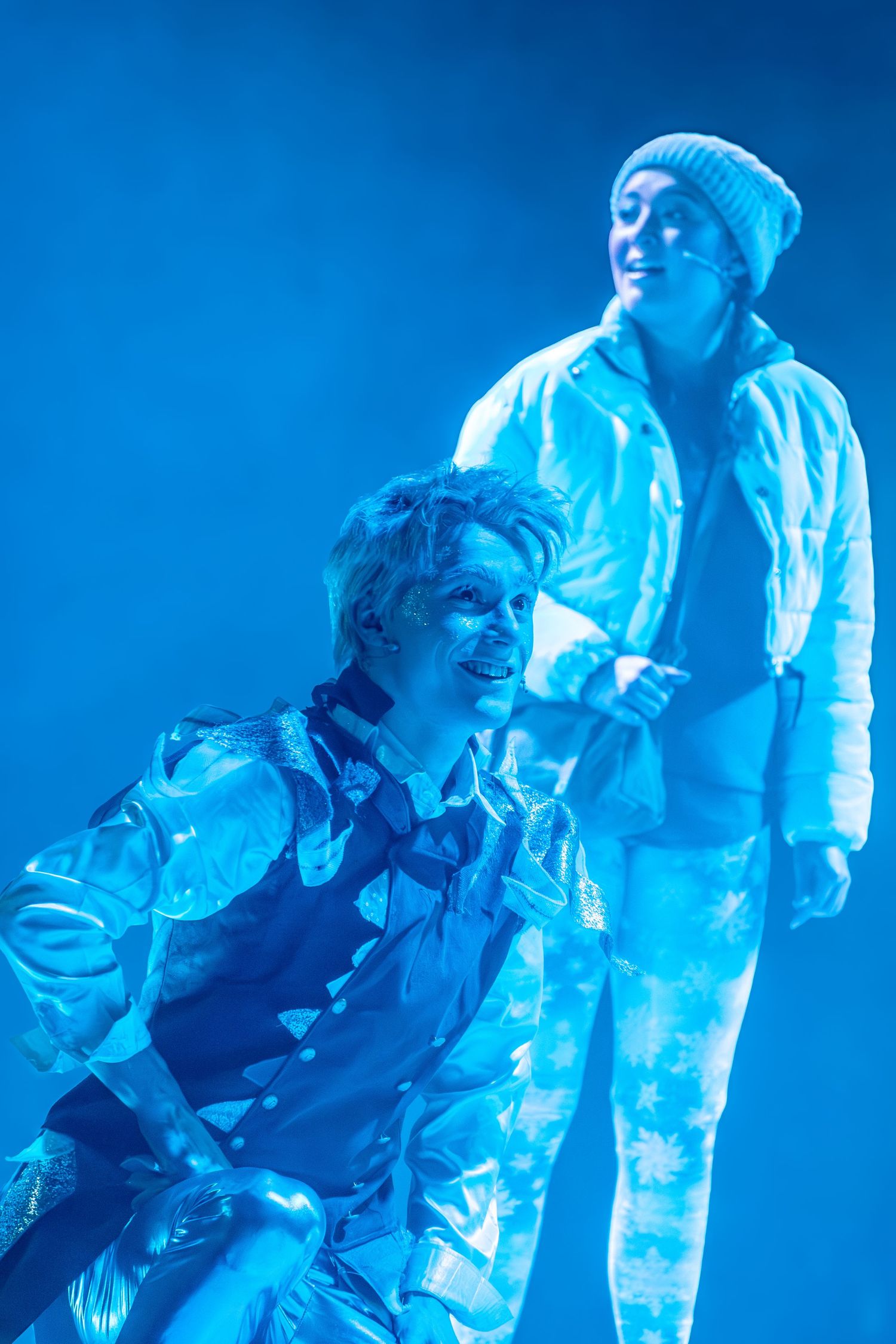Dancers perform an energetic sequence under intense blue stage lighting.