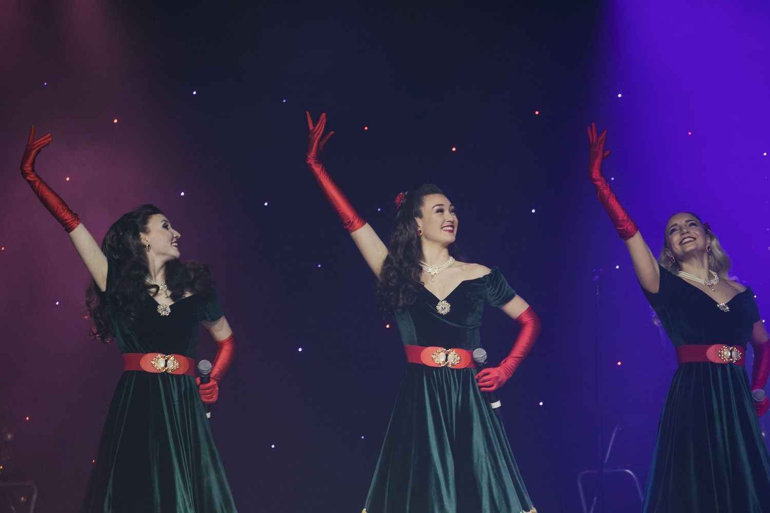 Performers in coordinated black dresses dance in formation under purple stage lights.