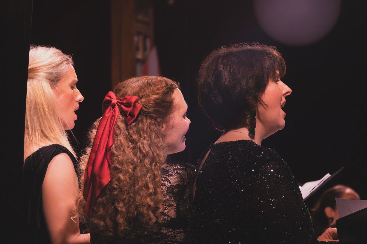 Choir performers dressed in black singing during a concert performance with dramatic lighting.