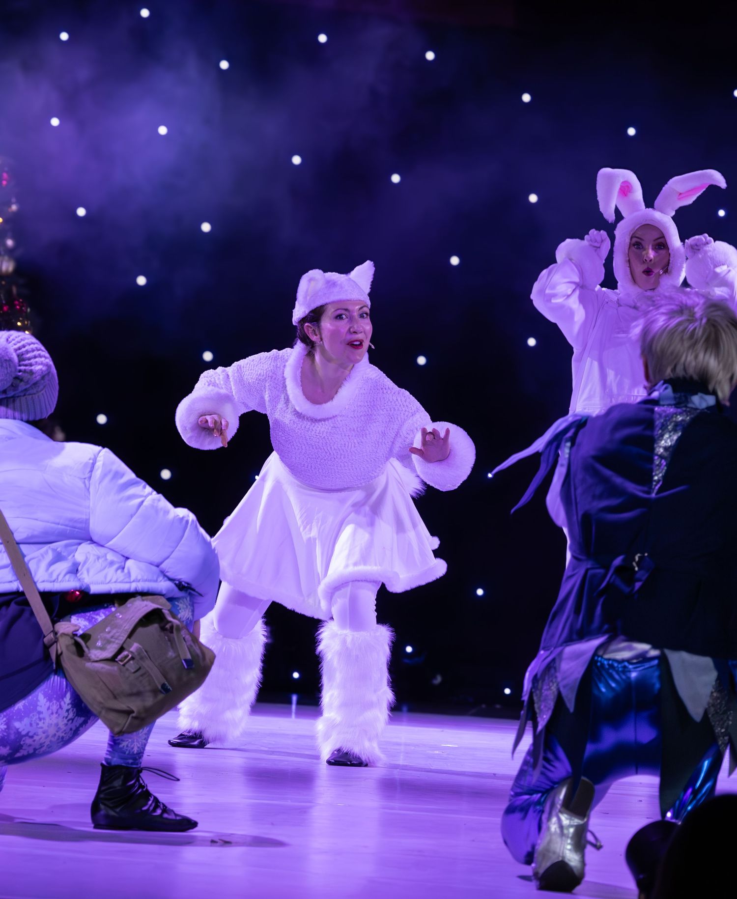 Performers in white costumes execute synchronized dance moves on an illuminated stage.