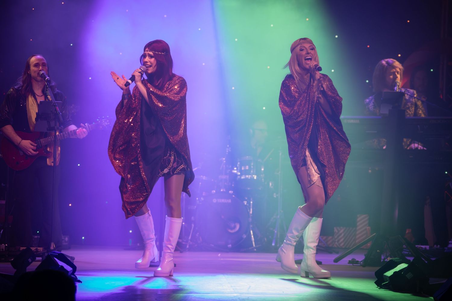 Dancers perform choreographed routine in matching costumes under dramatic stage lighting.