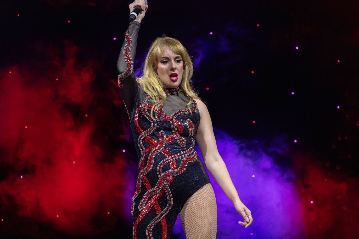A dramatic stage performance featuring a black and red costume against purple and red smoke effects.