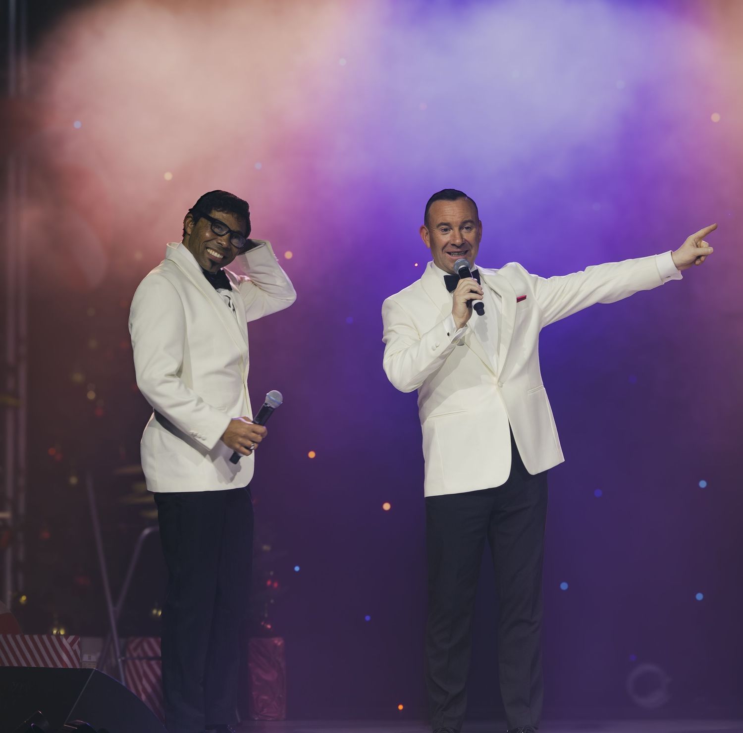 Performers in white jackets sing and gesture dramatically on purple-lit stage.