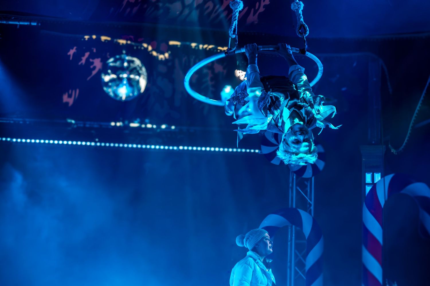 Acrobatic performers swing through the air on ropes during a theatrical production.