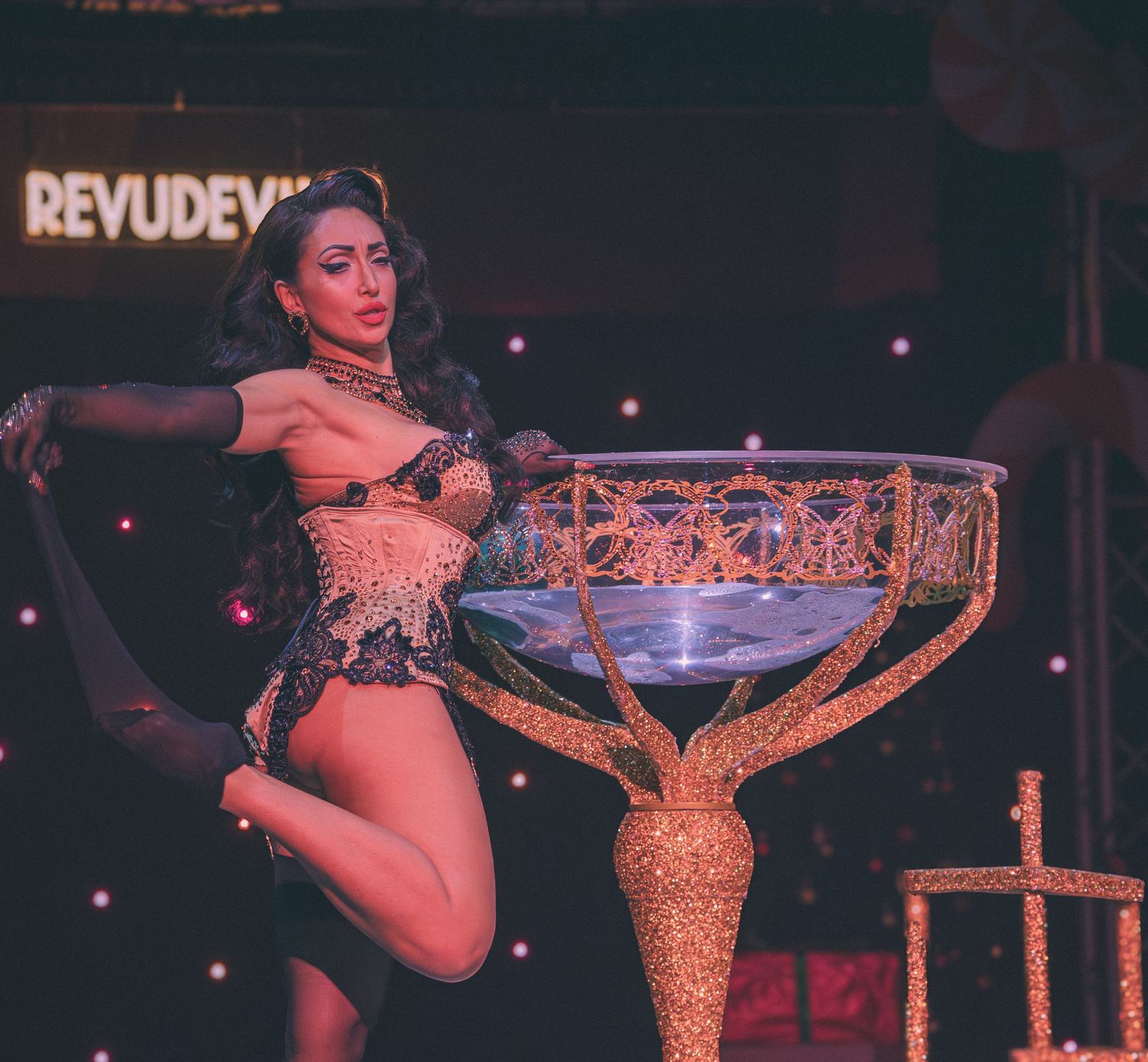 Burlesque stage performance featuring ornate golden prop and dramatic lighting.