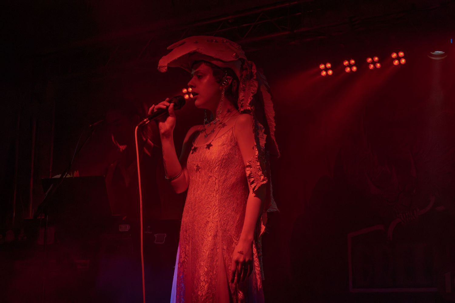 Concert stage illuminated with deep red lighting as performer stands in dramatic silhouette.