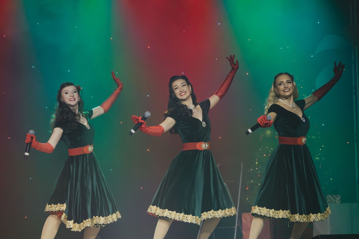 Dancers in matching dark dresses perform synchronized routine on colorfully lit stage.