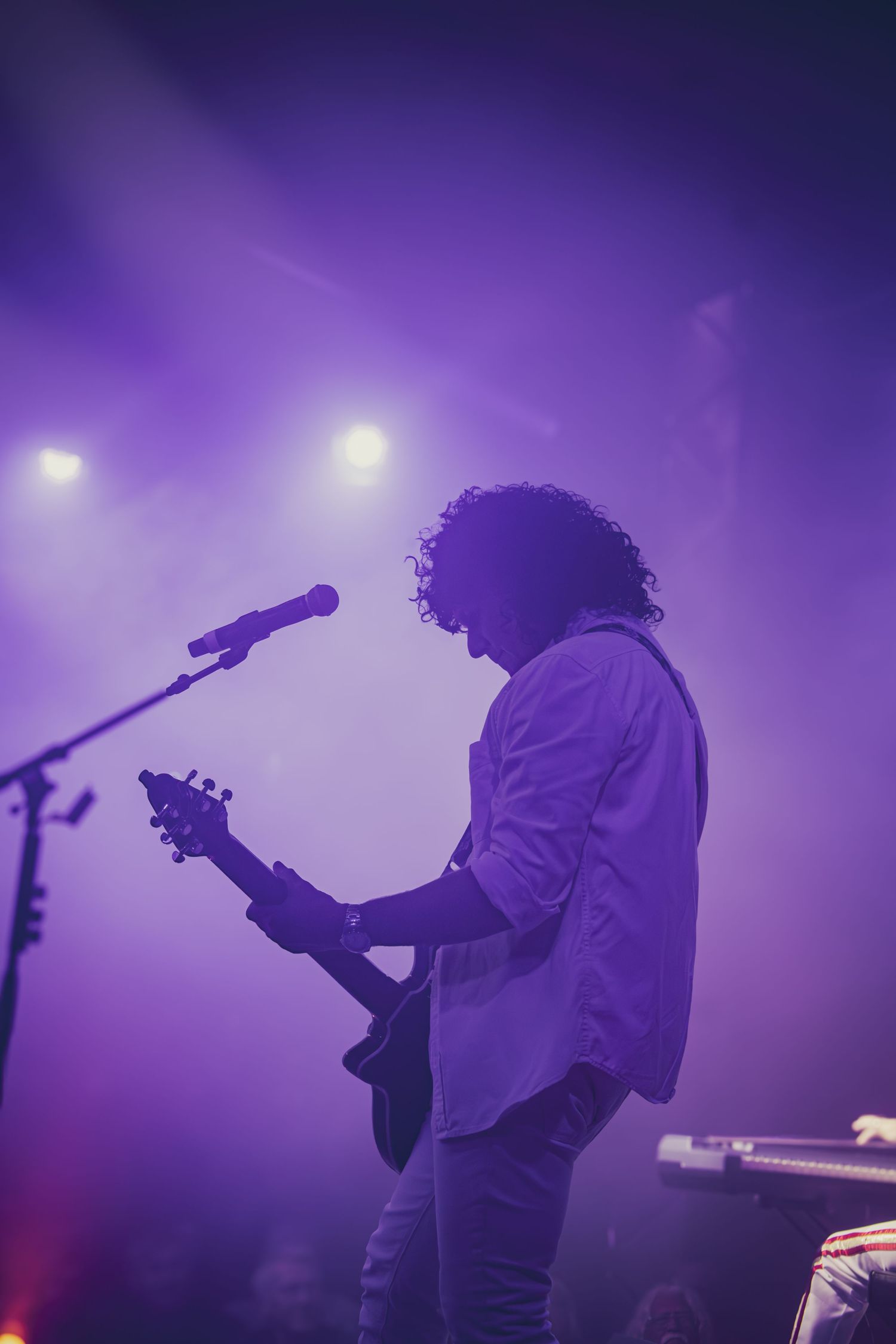 Silhouetted performers on stage with purple atmospheric lighting create dramatic concert ambiance.