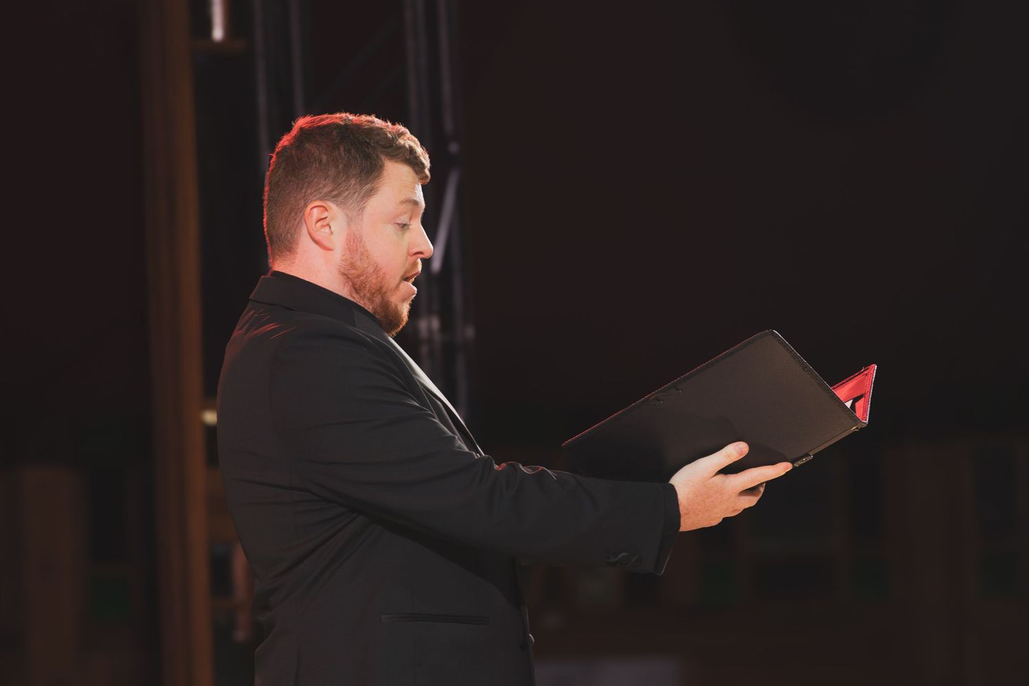 Performer reads from sheet music while singing during formal concert performance.
