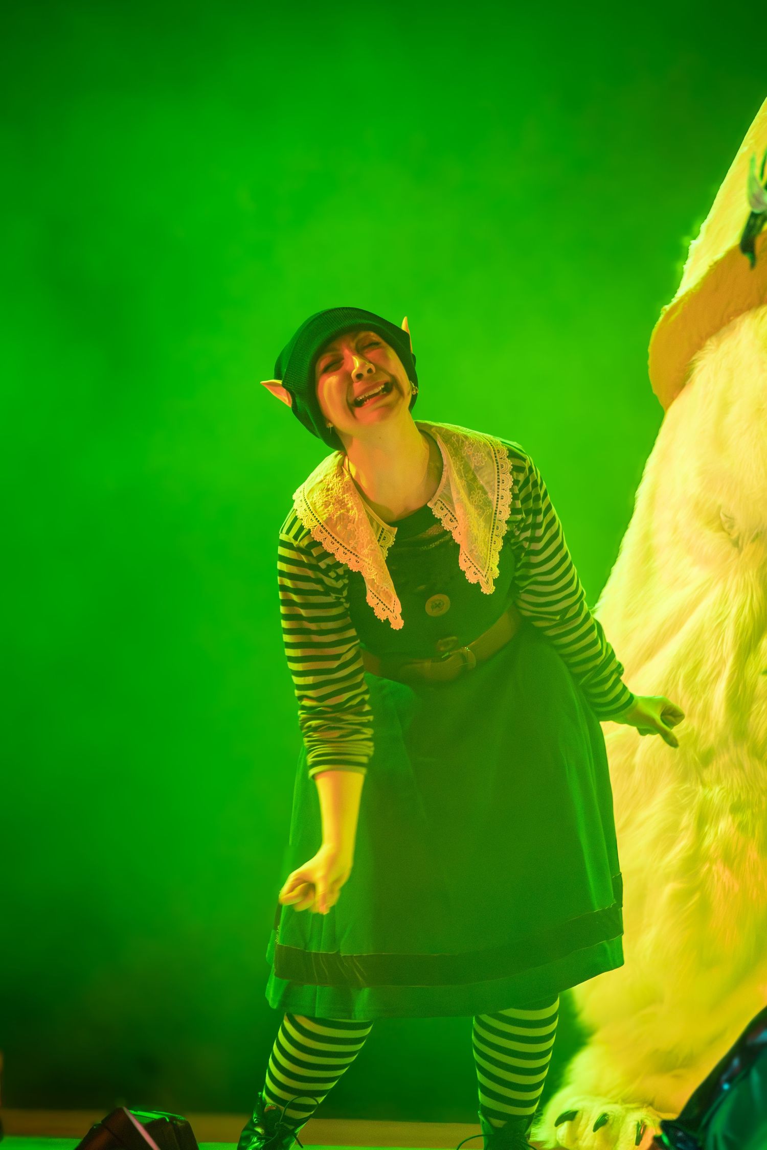 Performer in striped clothing dances against a bright green stage backdrop.