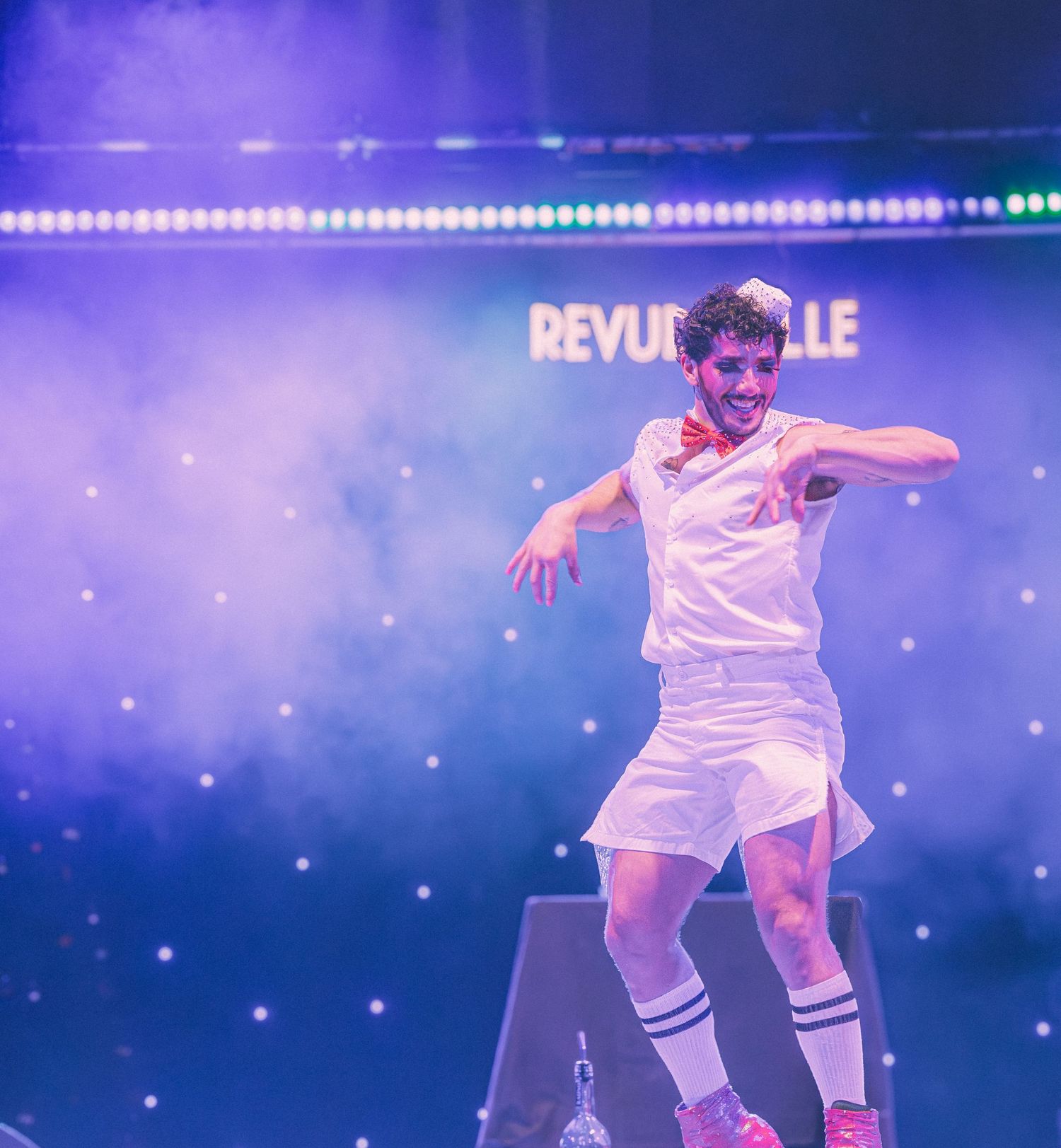 Performer in white outfit roller skating during theatrical show with blue stage lighting.