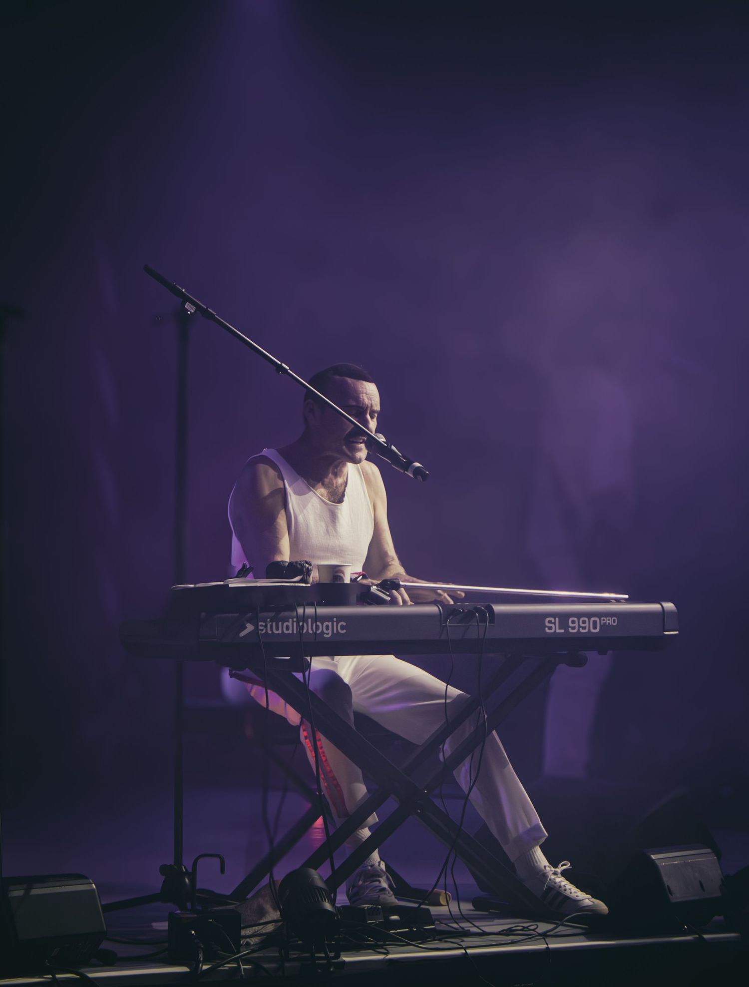 Musician performs on keyboard synthesizer in dramatic purple stage lighting during live concert performance.