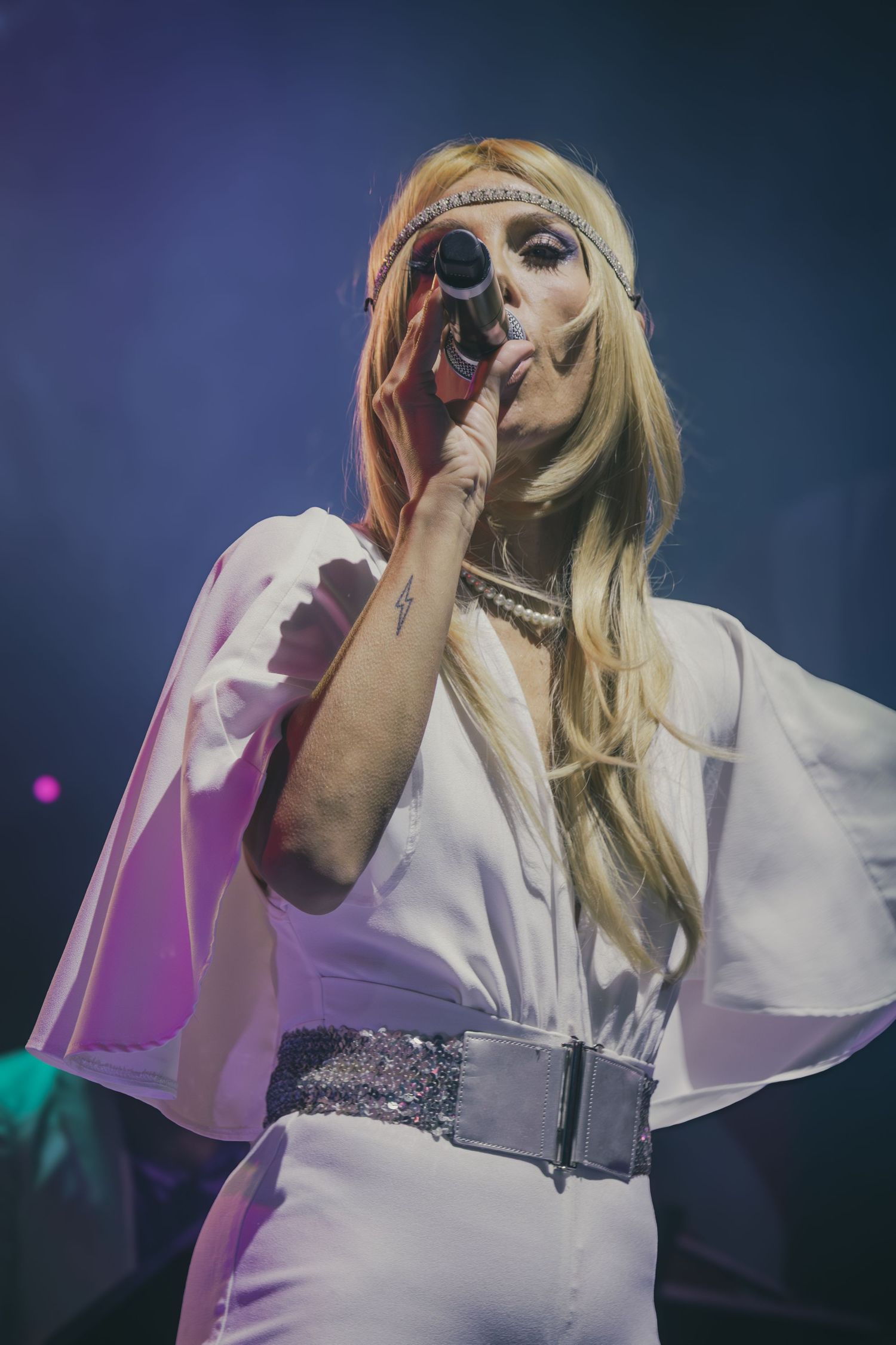Singer wearing white outfit with sparkly belt performs under blue stage lights.