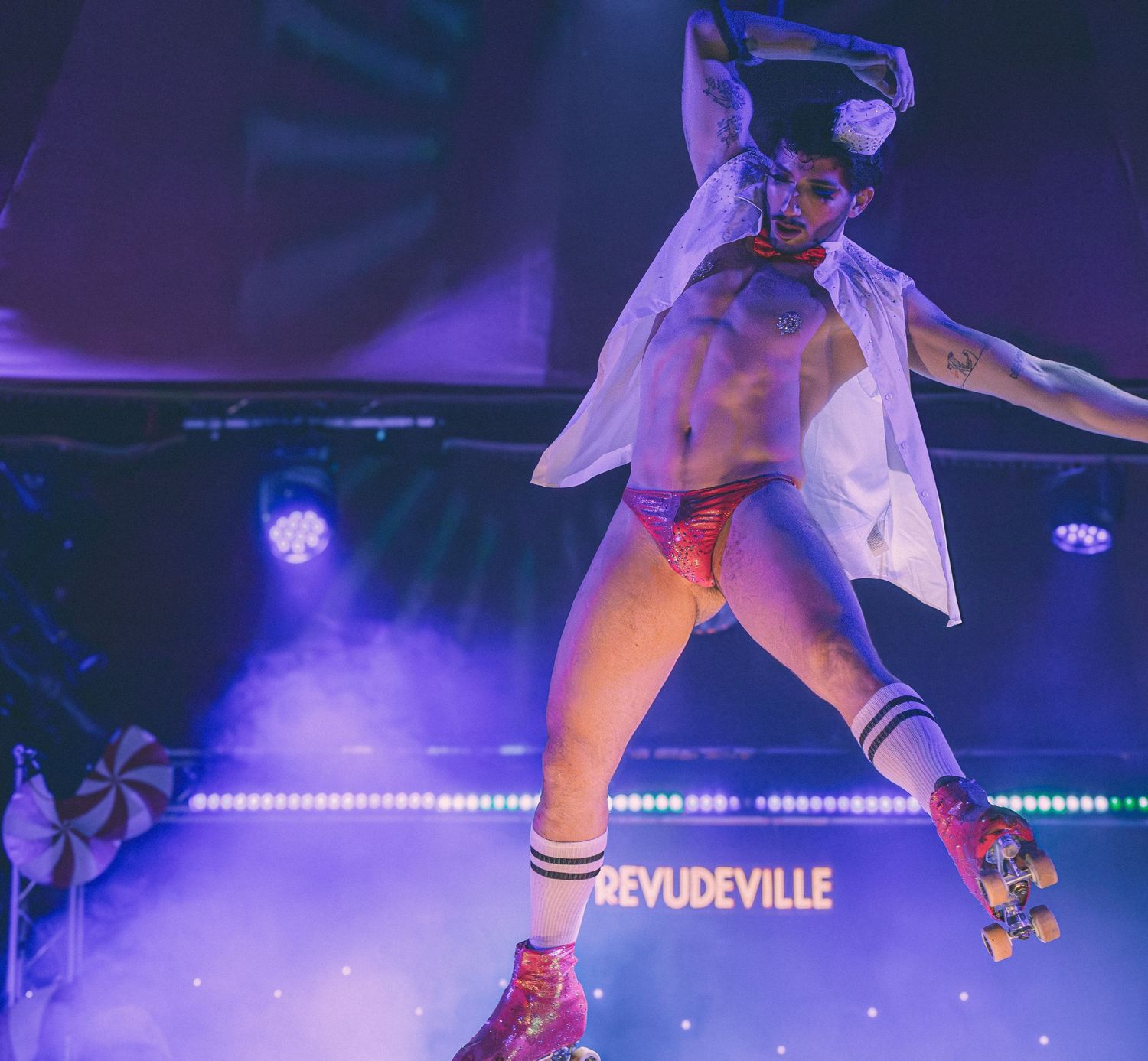 Performer in white outfit roller skating on stage with blue lighting and fog effects.