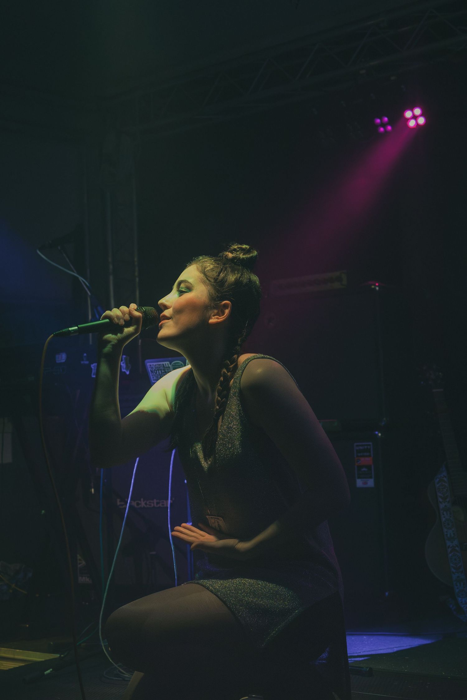 A performer in dark attire sings on stage under purple spotlights during a concert performance.