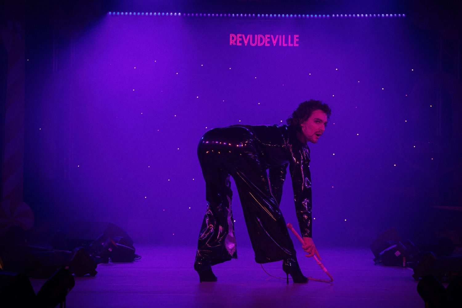 Dark silhouettes of performers against purple-lit stage with overhead lighting.