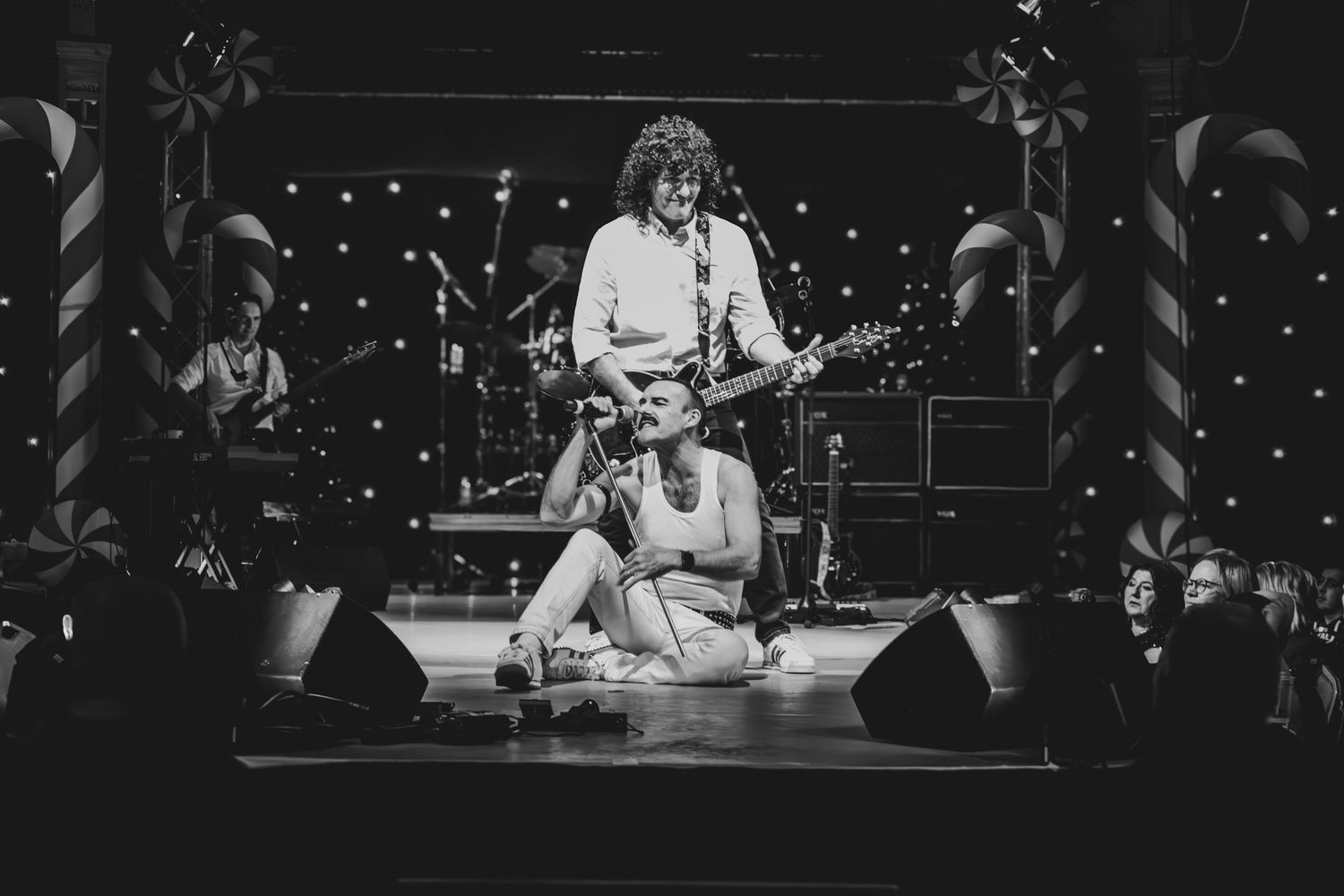Concert performers on stage with instruments and microphones in a dark venue with stage lighting.