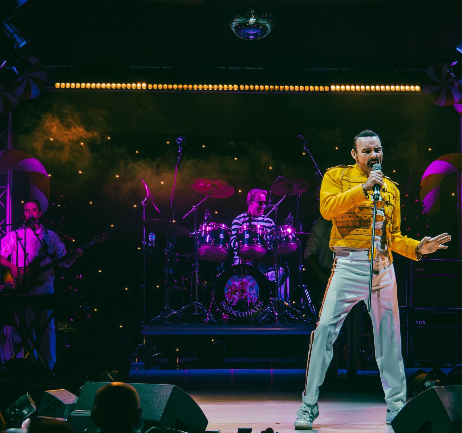 Dynamic concert performance on stage with dramatic lighting and colorful purple and yellow accents.