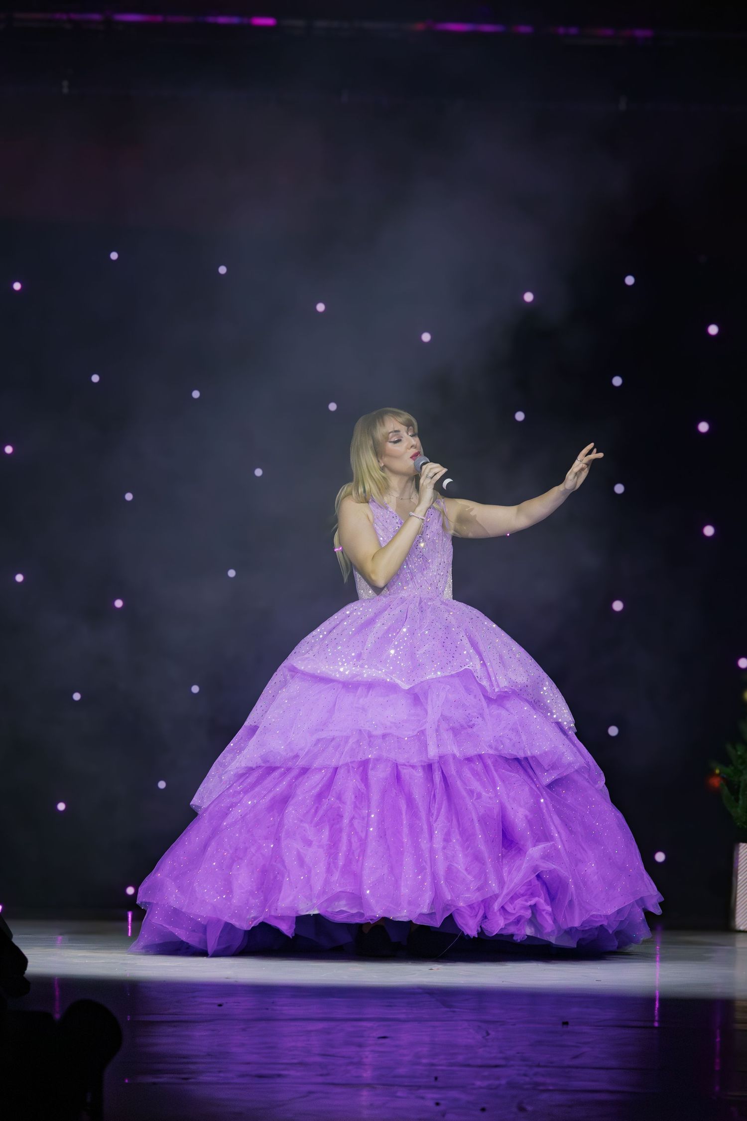 Performer wearing lavender ballgown during dramatic stage performance with starlit backdrop.