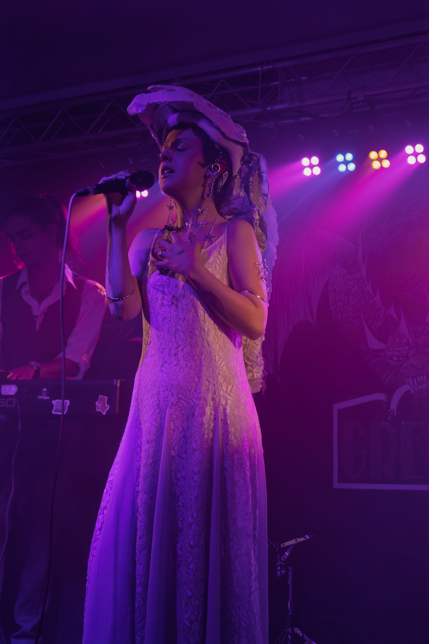 Musical performance on stage with purple and pink theatrical lighting creating an ethereal atmosphere.