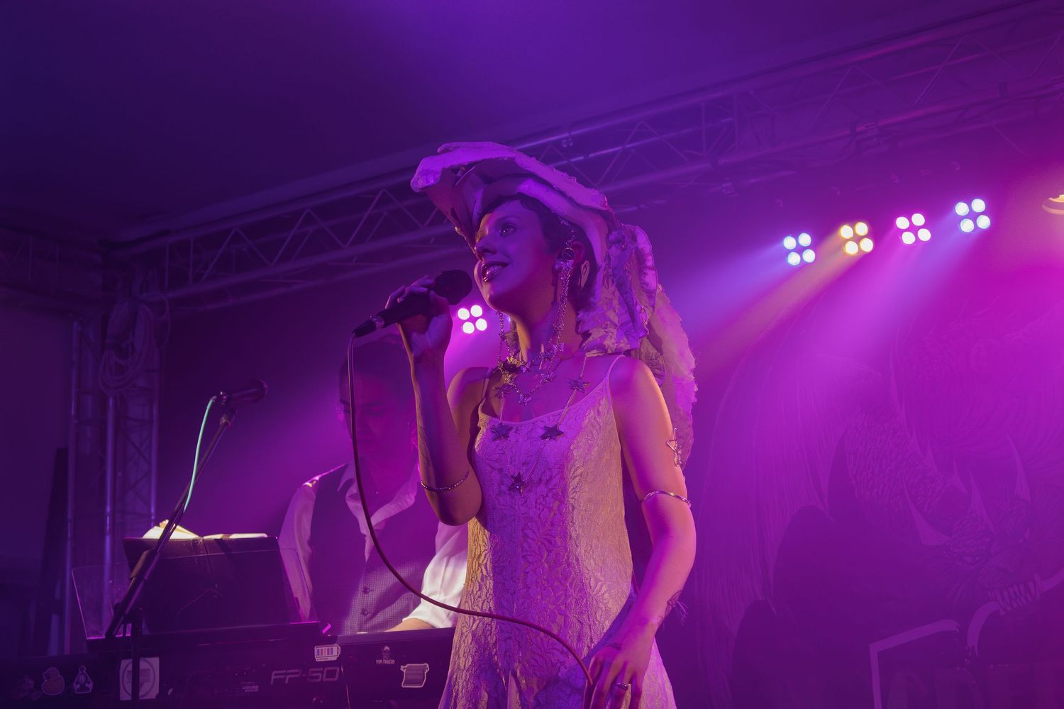 Concert performers on stage illuminated by vibrant purple lighting during a live music performance.