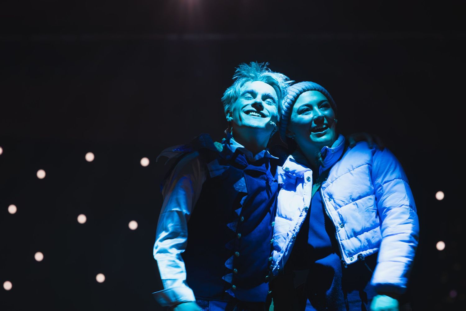 Performers in blue-lit costumes create dramatic silhouettes on a dark stage.