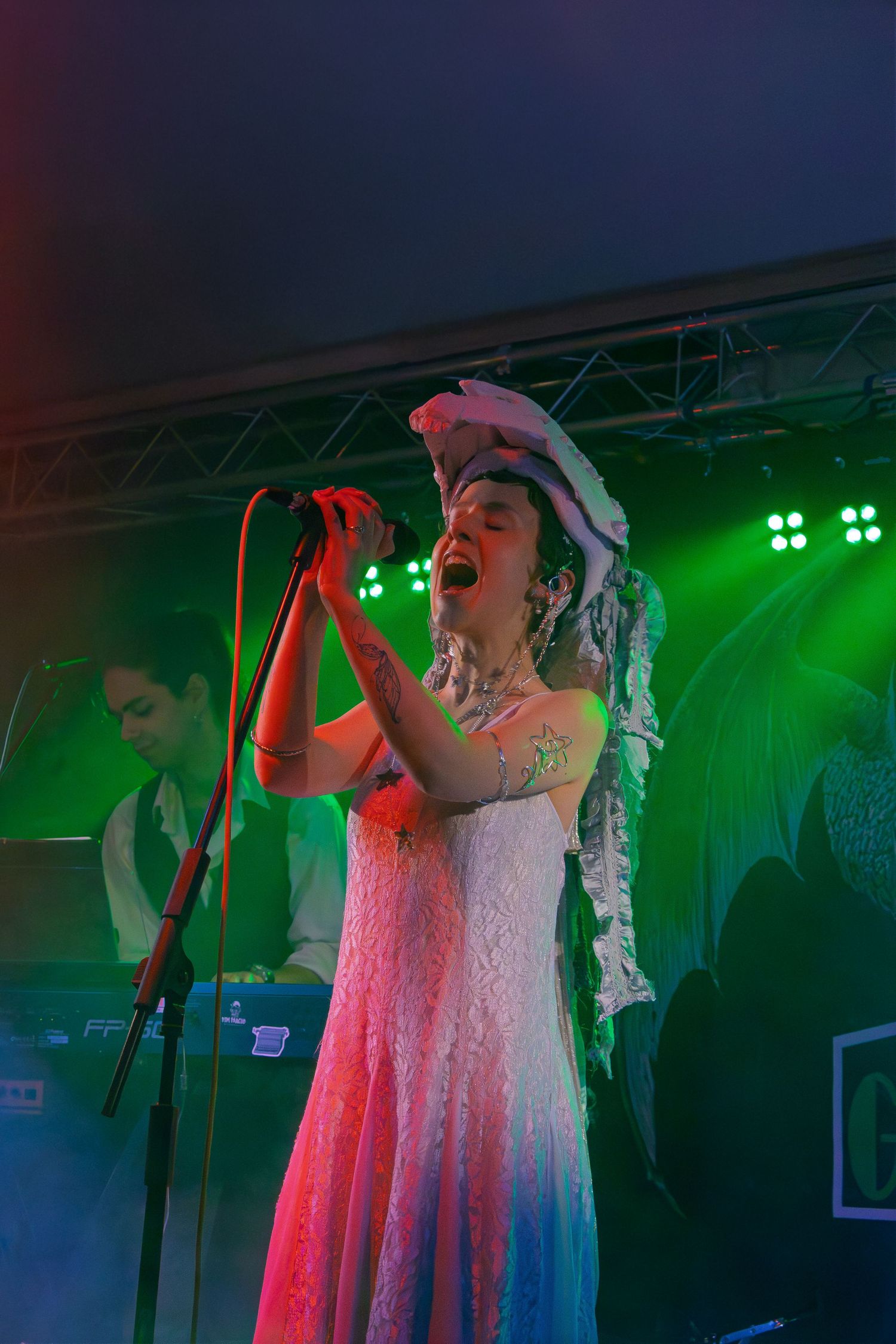 Concert performer singing on stage illuminated by dramatic green lighting and fog effects.