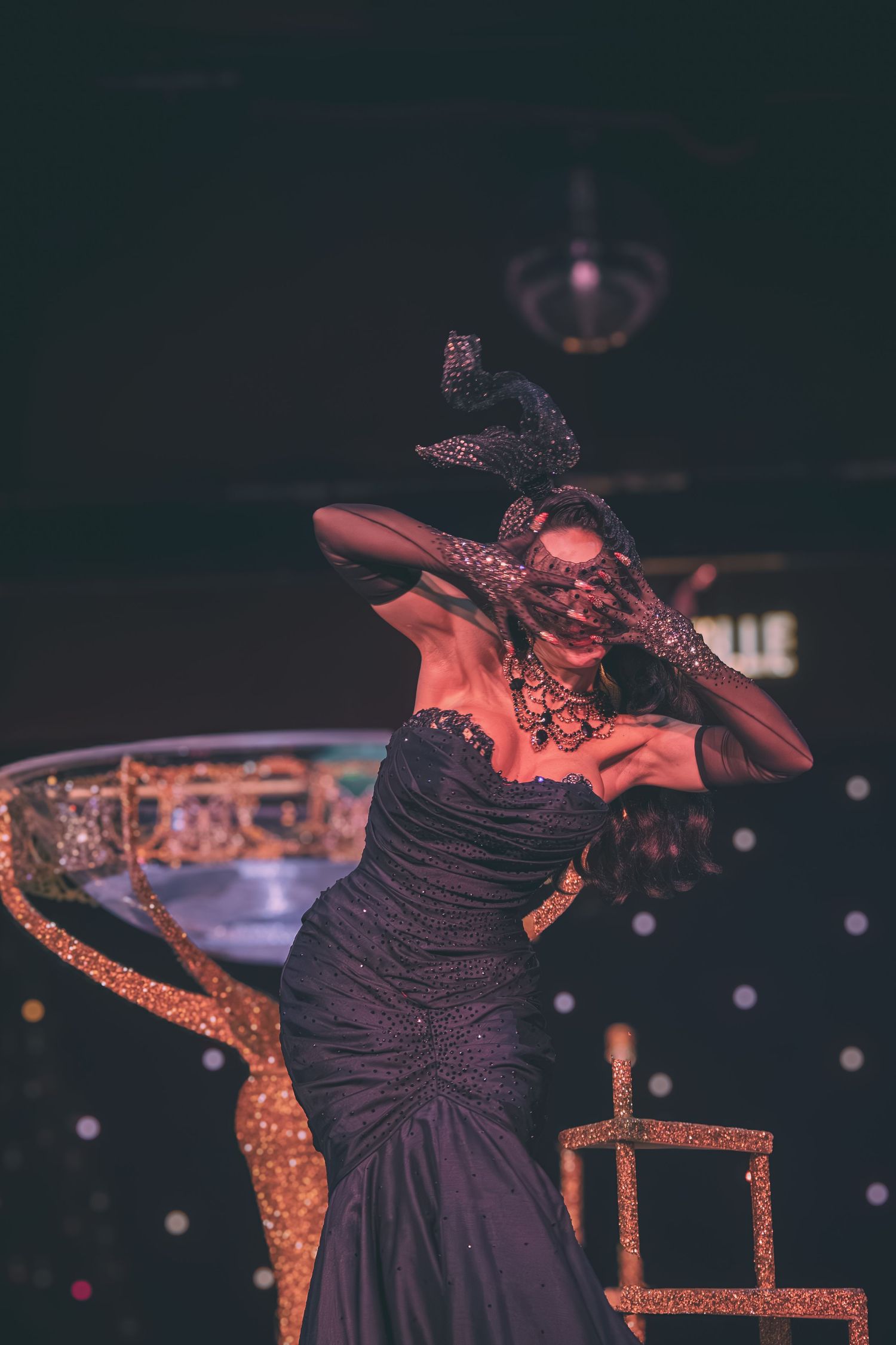 Dancer in black dress performs expressive movements near ornate golden stage decorations.