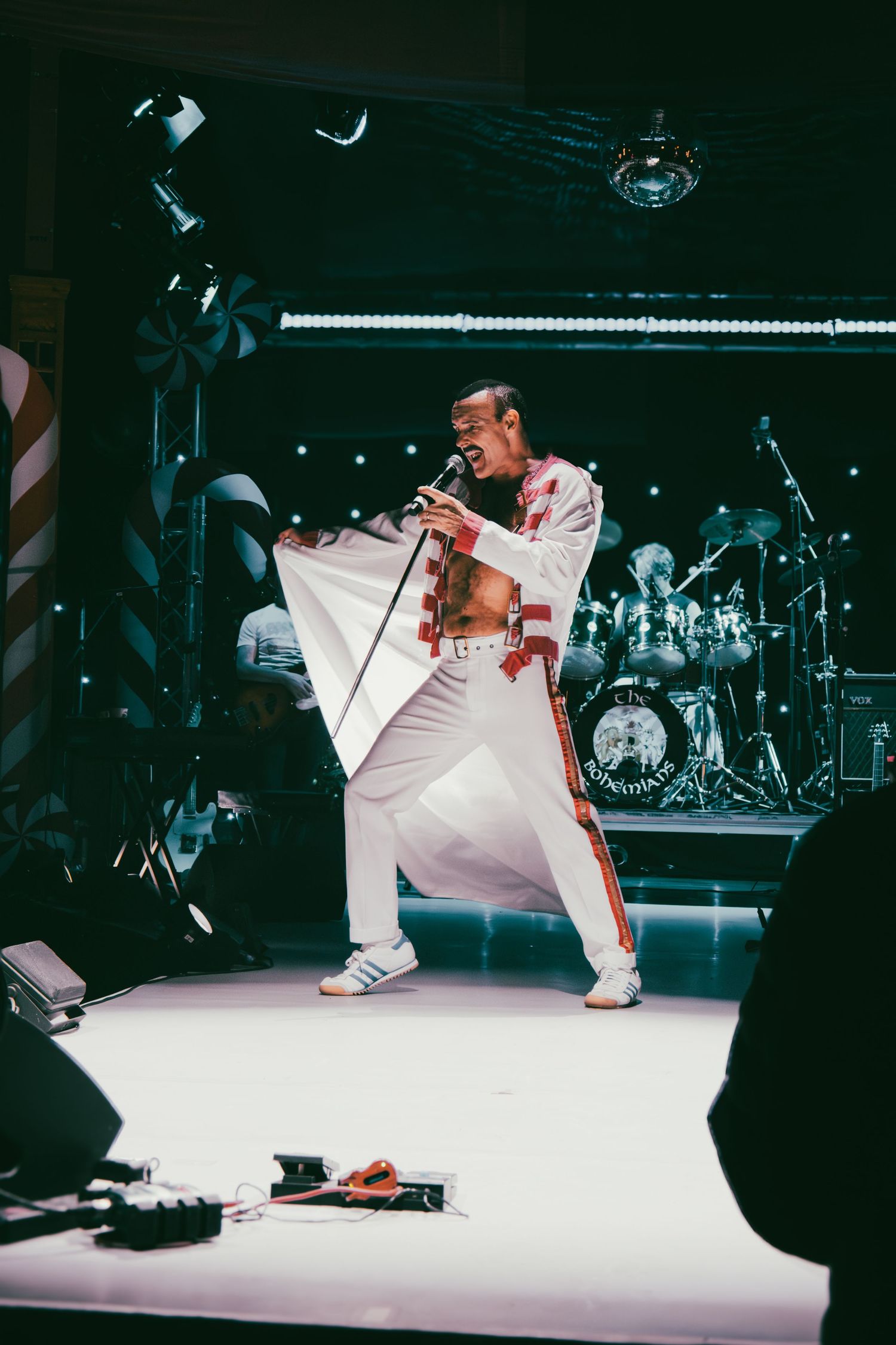 Dancers in white costumes perform acrobatic moves on illuminated stage floor.