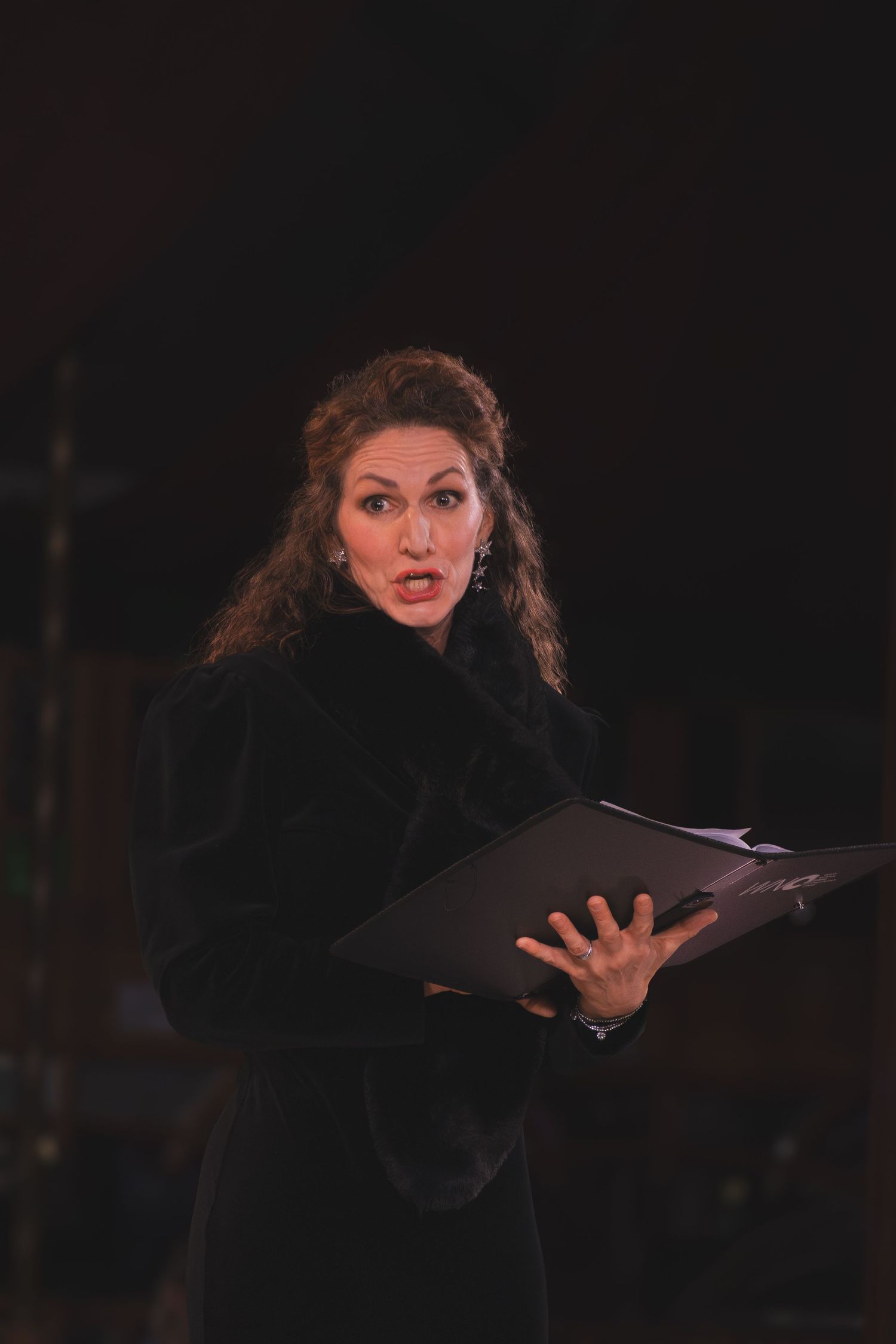 Performer in black holding a music book delivers an emotional solo performance on stage.