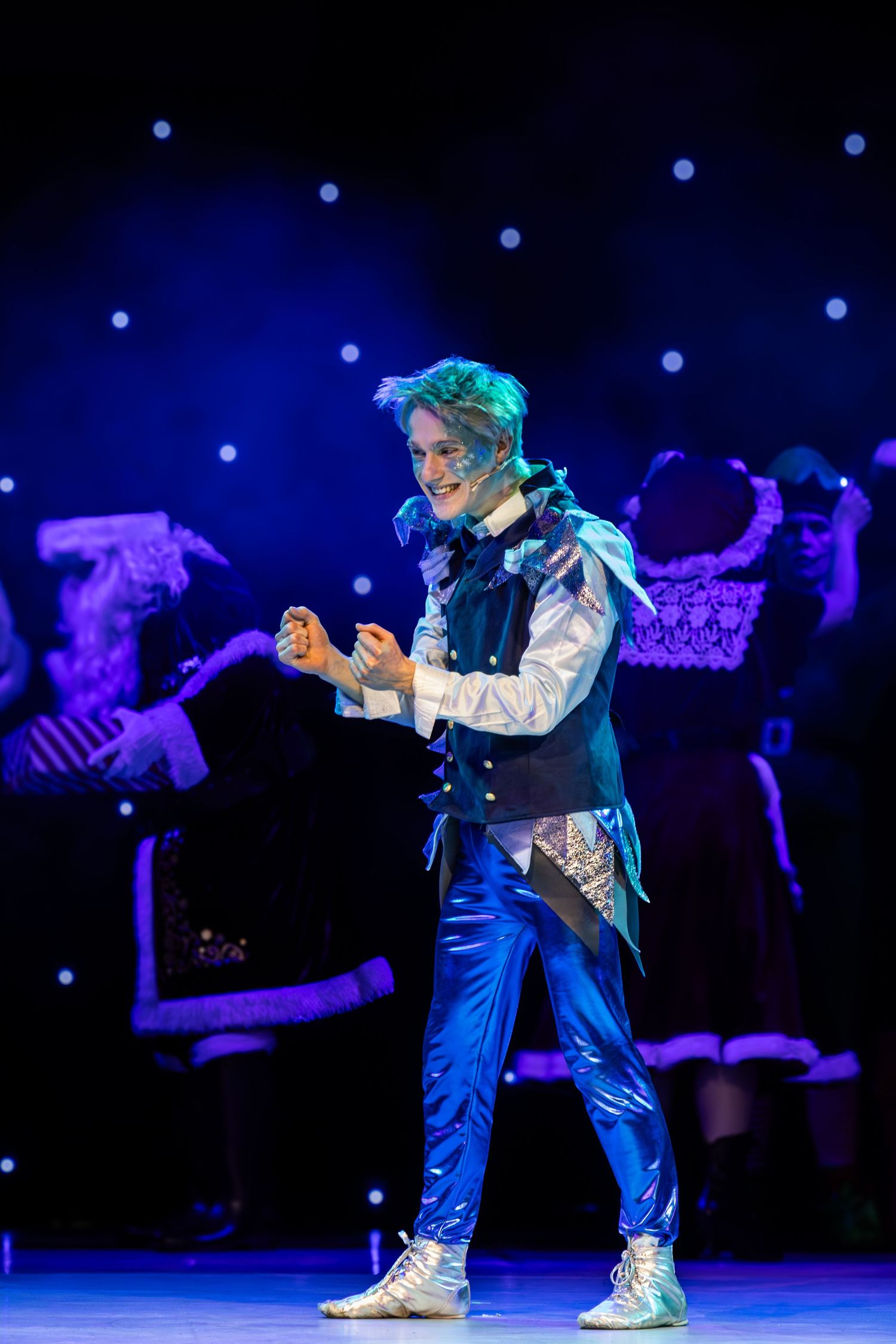 Dancer in blue overalls performs dynamic moves on a dark stage with blue spotlights.