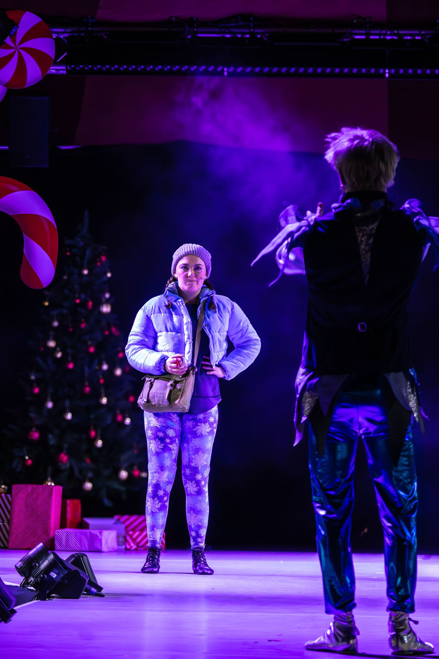 Stage performers in winter outfits under purple theatrical lighting.