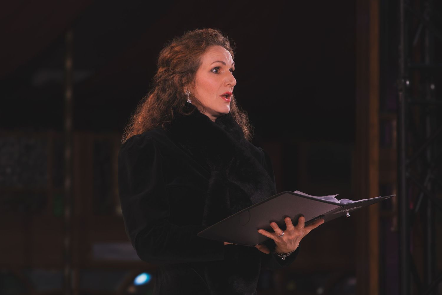 Performers in dark attire singing on stage during an evening concert performance.