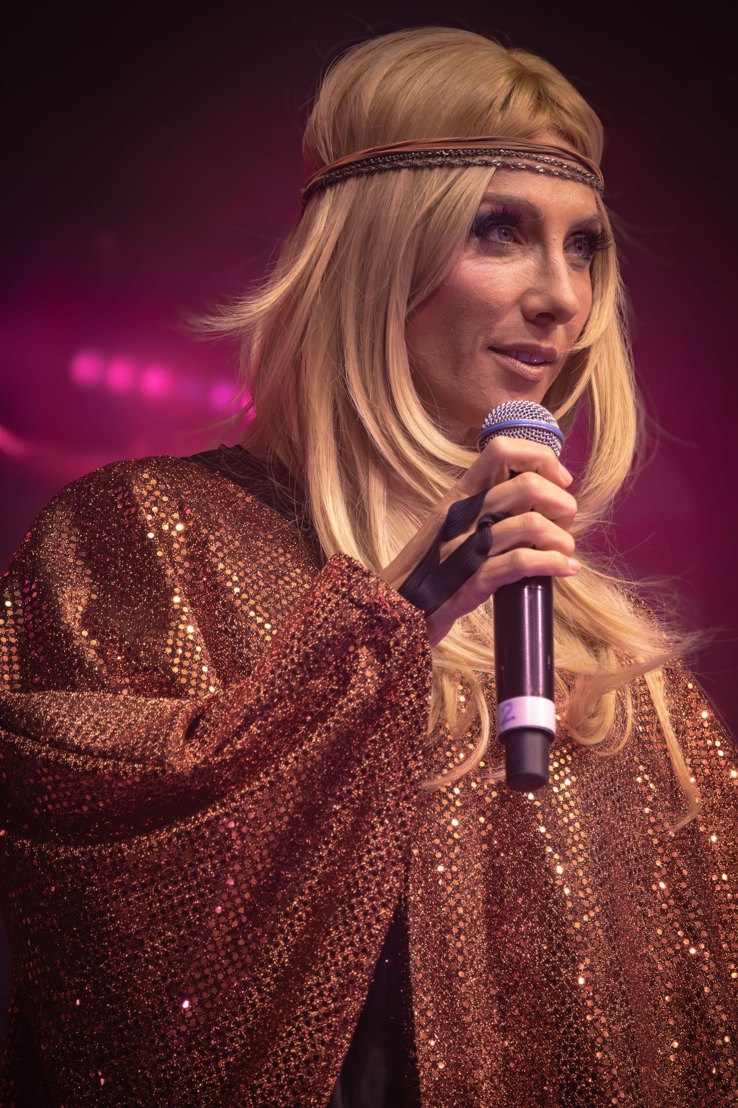 Singer wearing sparkly copper dress and headband performing under purple stage lights.