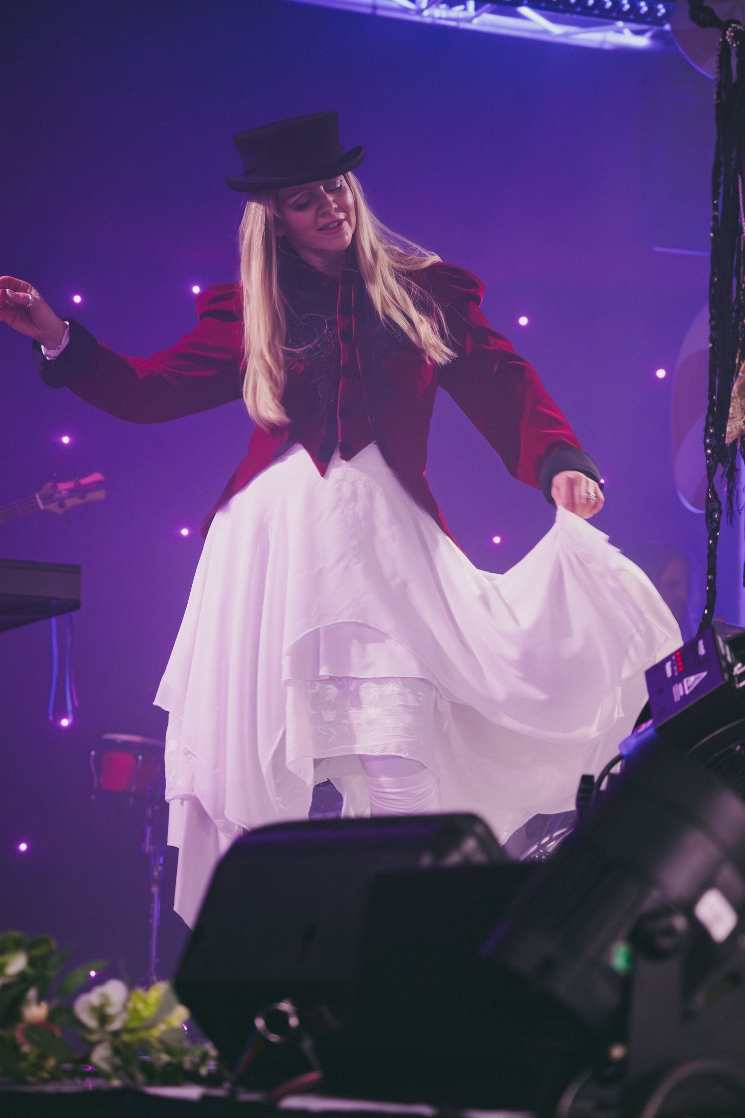 Stage performer in white flowing dress moves energetically under purple concert lighting.