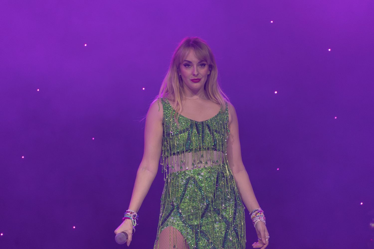 Concert performer in green dress on purple-lit stage with dramatic lighting effects.