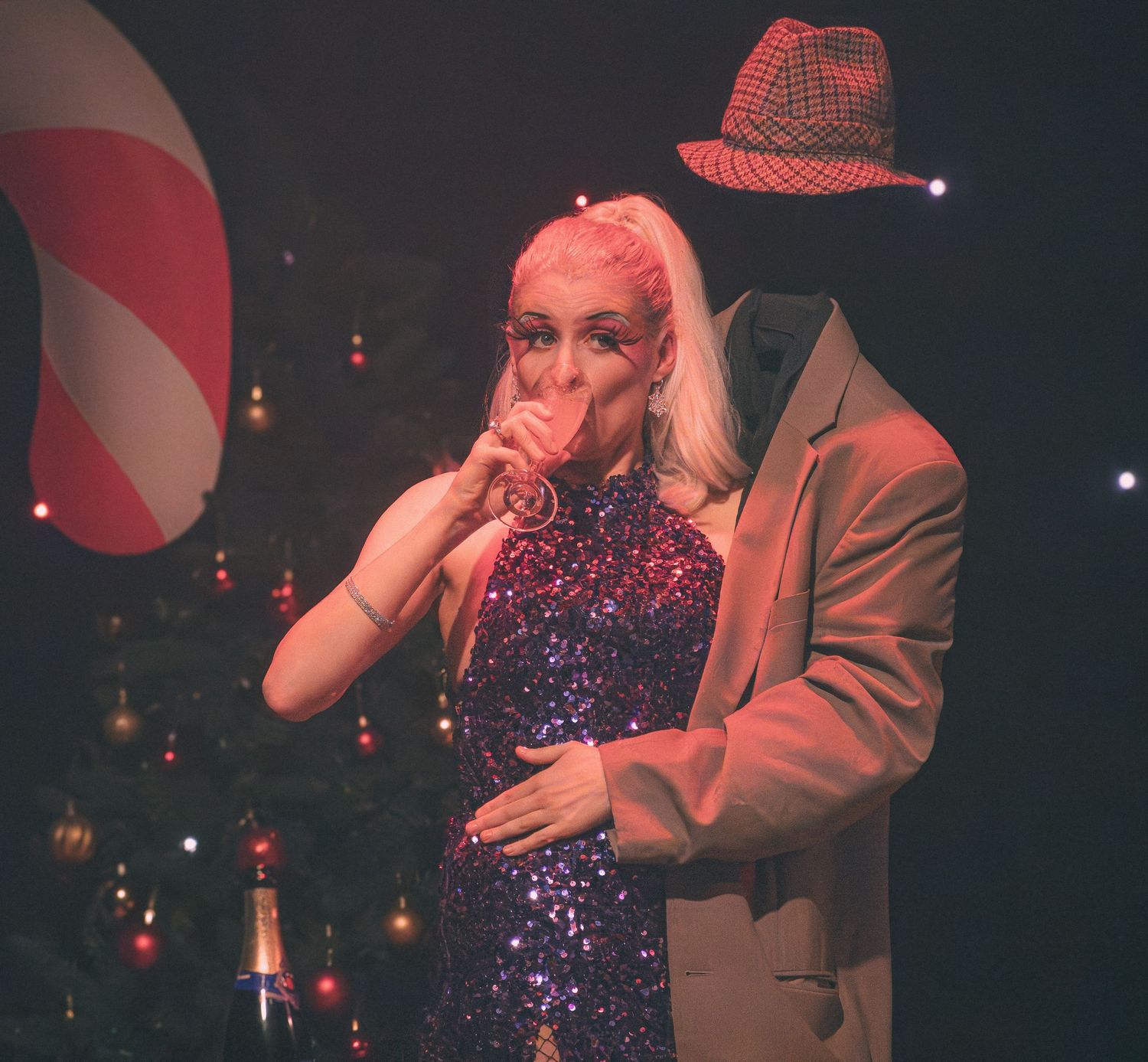 Cabaret show performers in sparkly outfits on dimly lit stage with red lighting.