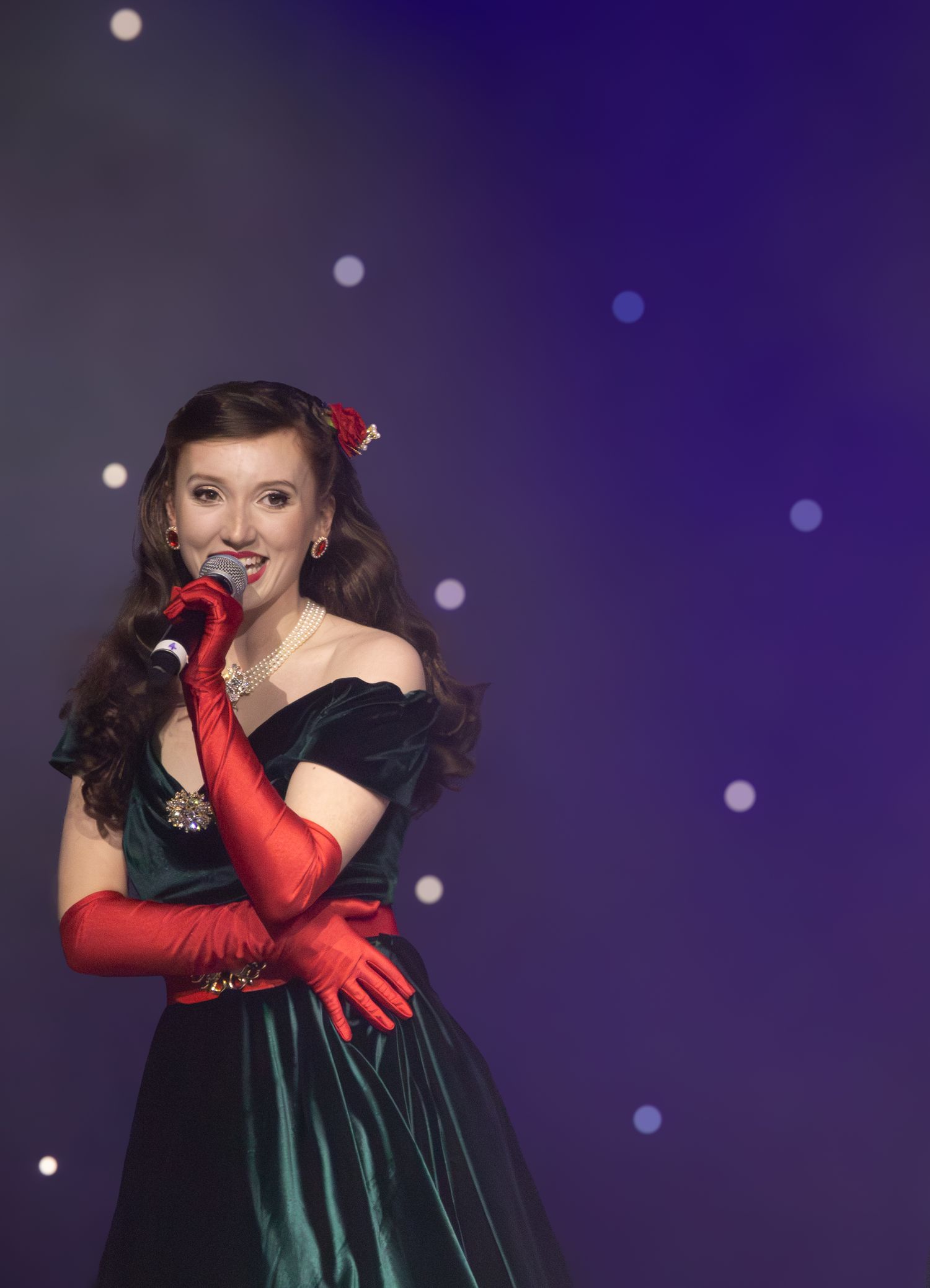A performer in an elegant dress and red gloves strikes dramatic poses on a purple-lit stage.