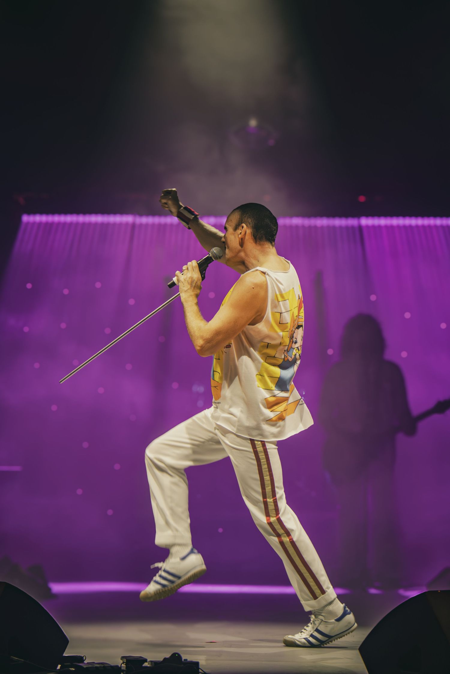 Performer in white and gold outfit strikes dynamic poses on stage with purple lighting effects in background.
