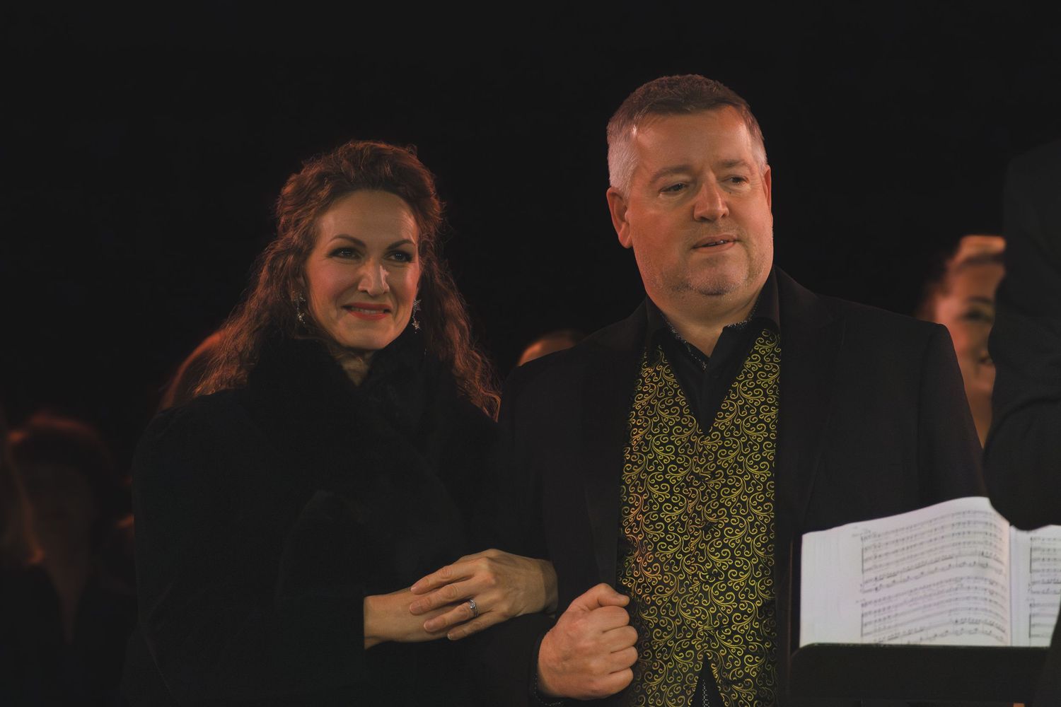 Performers in formal attire holding sheet music during a concert performance.
