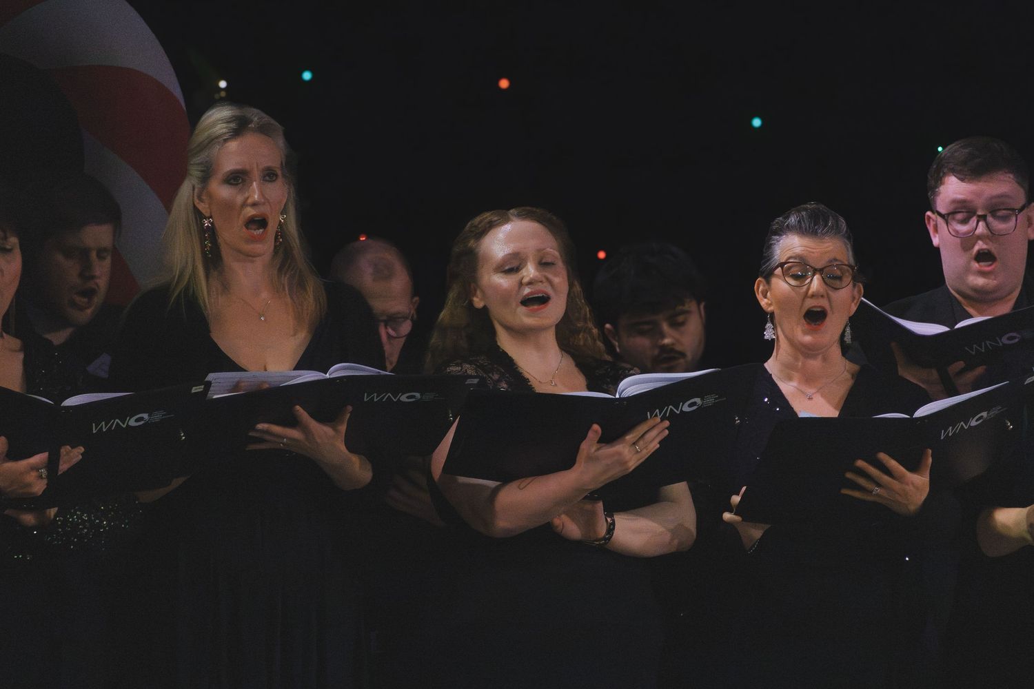 Choir members in black attire sing expressively during evening performance.