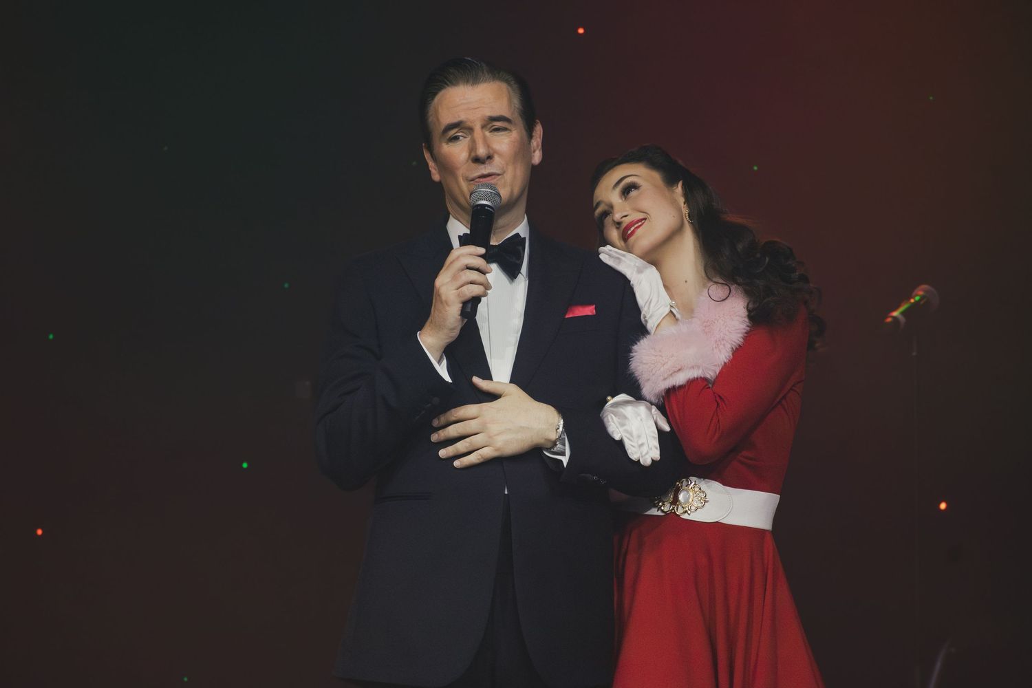 Stage performers in formal wear dance during theatrical holiday production.